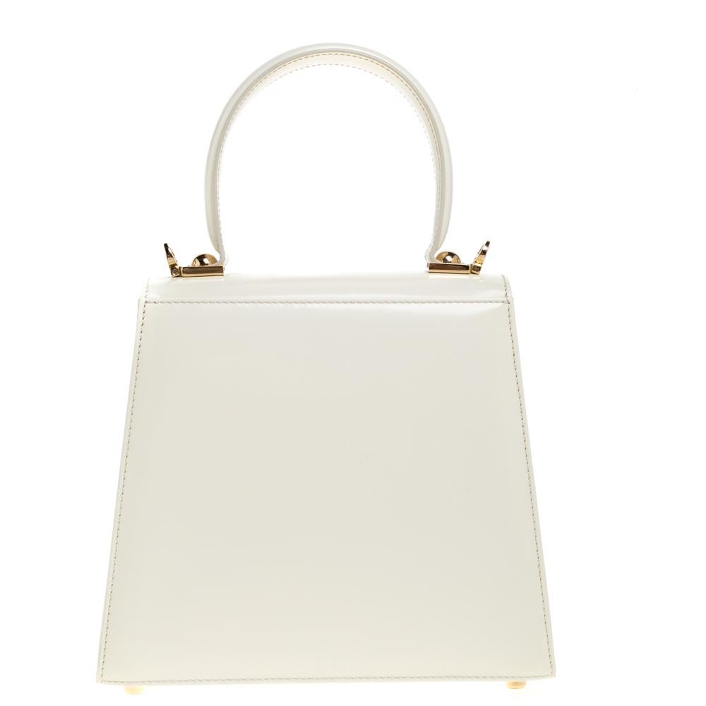 Spread elegance with this cream patent leather bag from Salvatore Ferragamo that is accented with the iconic Gancini bit in gold-tone at the front flap. With a classic silhouette, the 'Kelly' top handle bag becomes perfect to tote at work. The