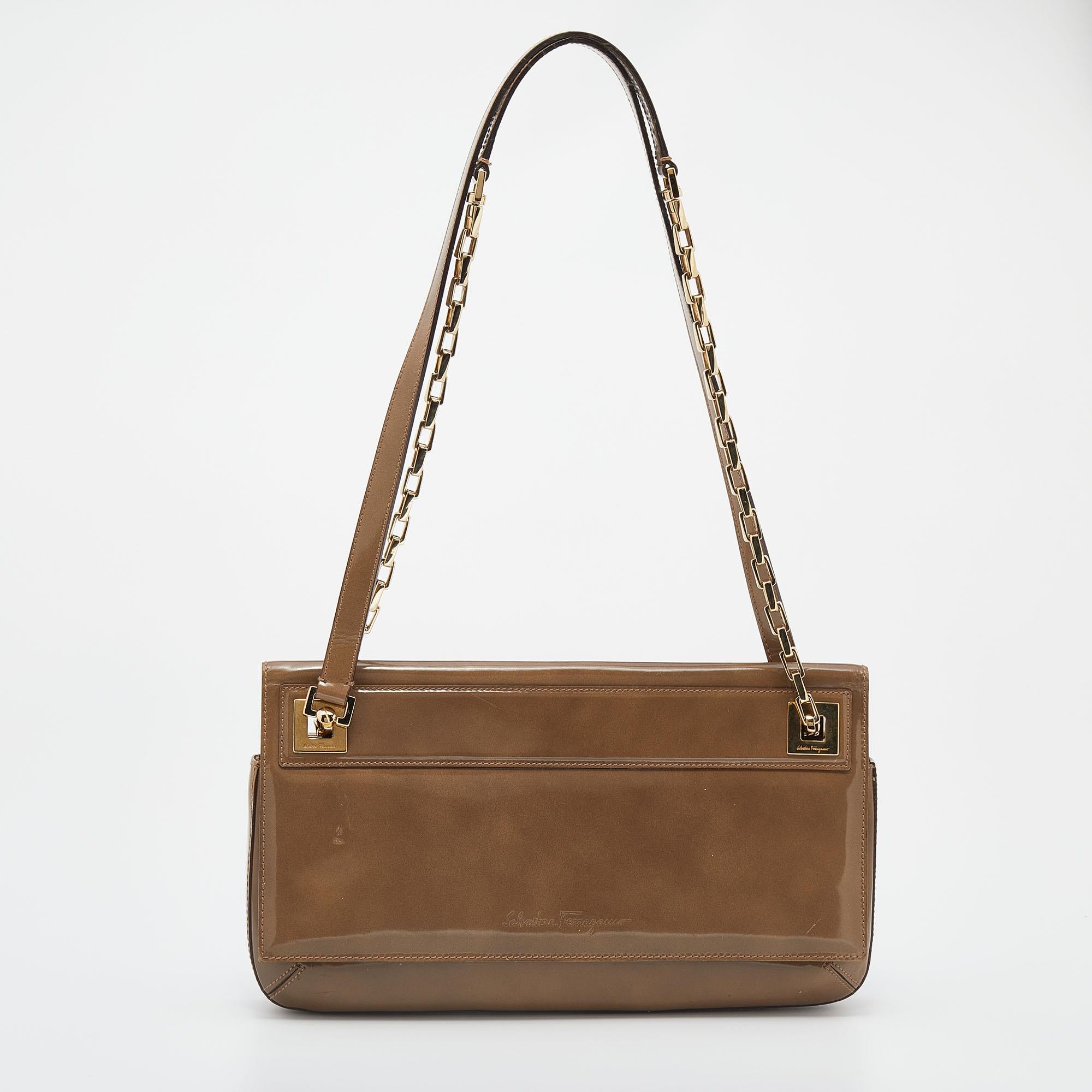 Elegance meets luxury in this shoulder bag from the House of Salvatore Ferragamo. It is created using dark-beige patent leather and has a roomy Alcantara-lined interior, gold-tone hardware, and a 30 cm handle drop. This stunning bag will elevate the