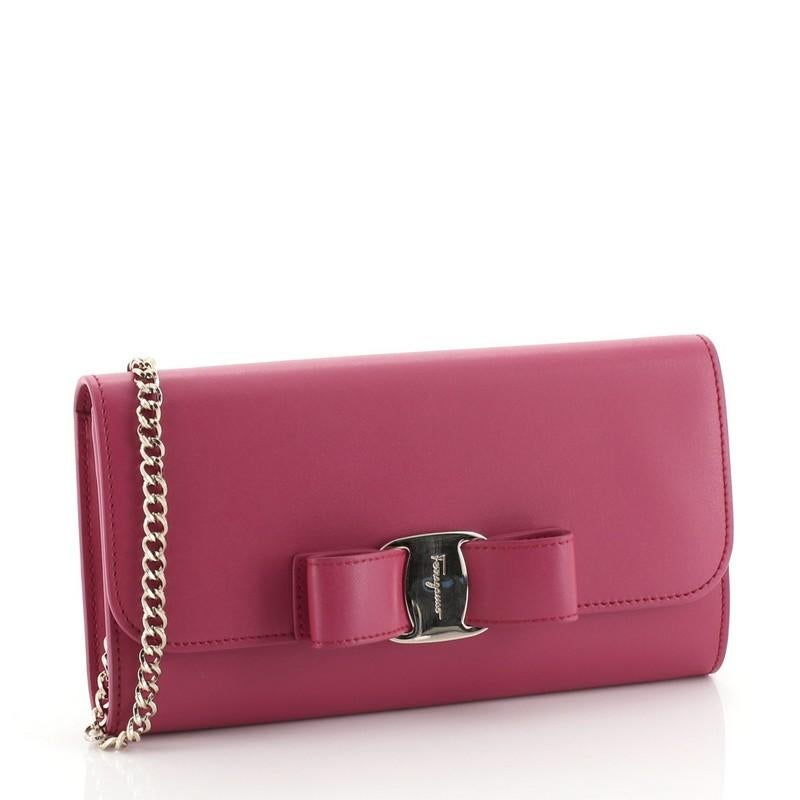 This Salvatore Ferragamo Miss Vara Chain Wallet Saffiano Leather, crafted in pink saffiano leather, features a long chain strap, Vara-shoe pleated bow design, and gold-tone hardware. Its snap closure opens to a neutral fabric and white leather