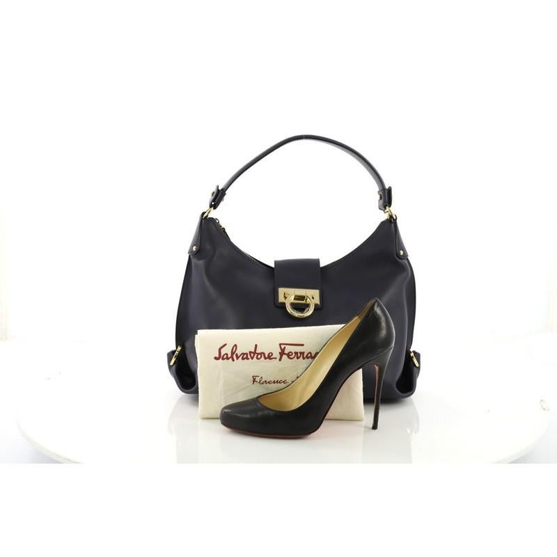 This Salvatore Ferragamo New Fanisa Hobo Leather Small, crafted in navy leather, features a single looped leather shoulder strap, accented with gold Gancini rings on both sides, and gold-tone hardware. Its flip-lock Gancini and zip closure opens to