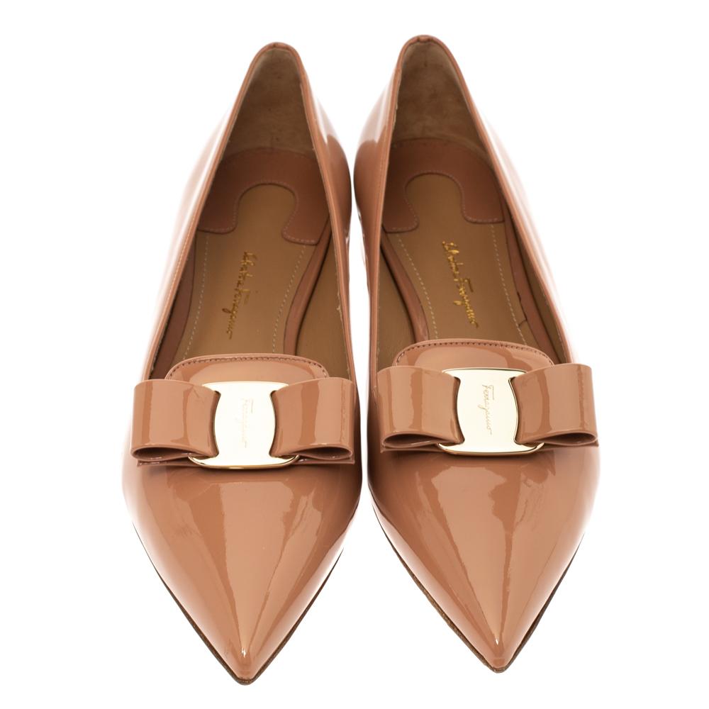 These Alice ballet flats by Salvatore Ferragamo are stunning and exude sophistication. Crafted from glossy peach-hued patent leather, they are styled with pointed toes. They flaunt the signature bows on the uppers and gold-tone hardware. They are