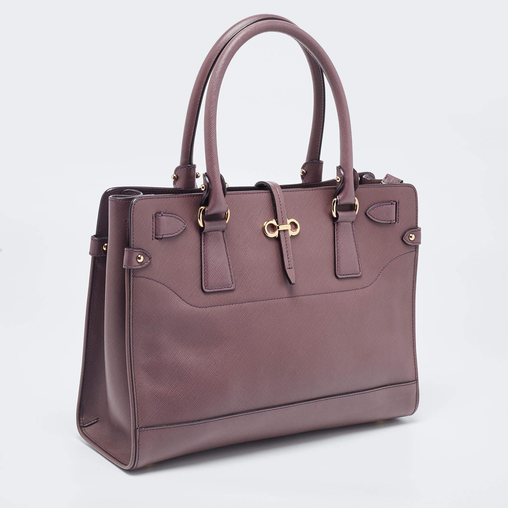 Crafted from leather, this plum Salvatore Ferragamo tote has a little lock-in flap and a spacious fabric interior. The bag is equipped with two handles and protective metal feet. Swing this beauty on your busy days as it is well-made and handy.

