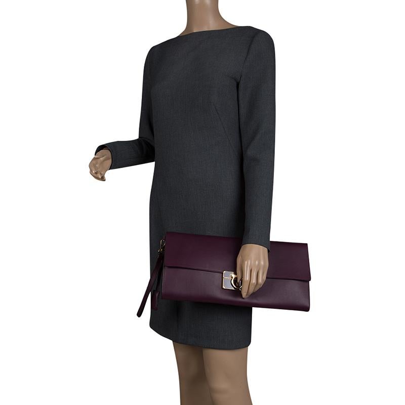 Finely crafted from leather, and shining with beauty is this beautiful clutch by Salvatore Ferragamo. It has been crafted from leather and designed in a purple shade with their signature Gancio detailed on the flap. Complete with leather insides and