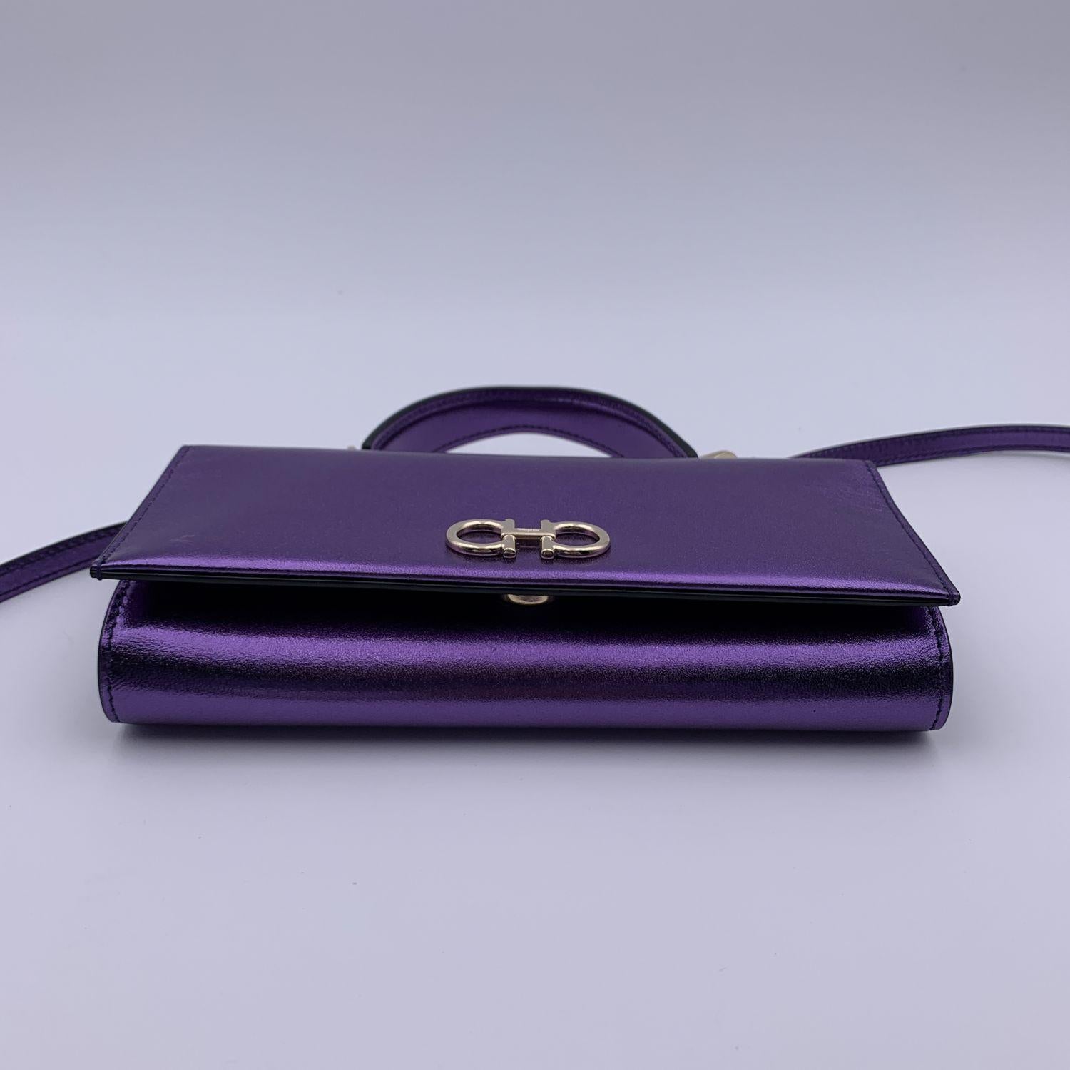 Salvatore Ferragamo 'The Gancini' Mini Bag in purple leather with metallic finish. Flap with magnetic button closure on the front. Silver metal signature Gancini logo on the front. Top handle and removable shoulder strap. Salvatore Ferragamo