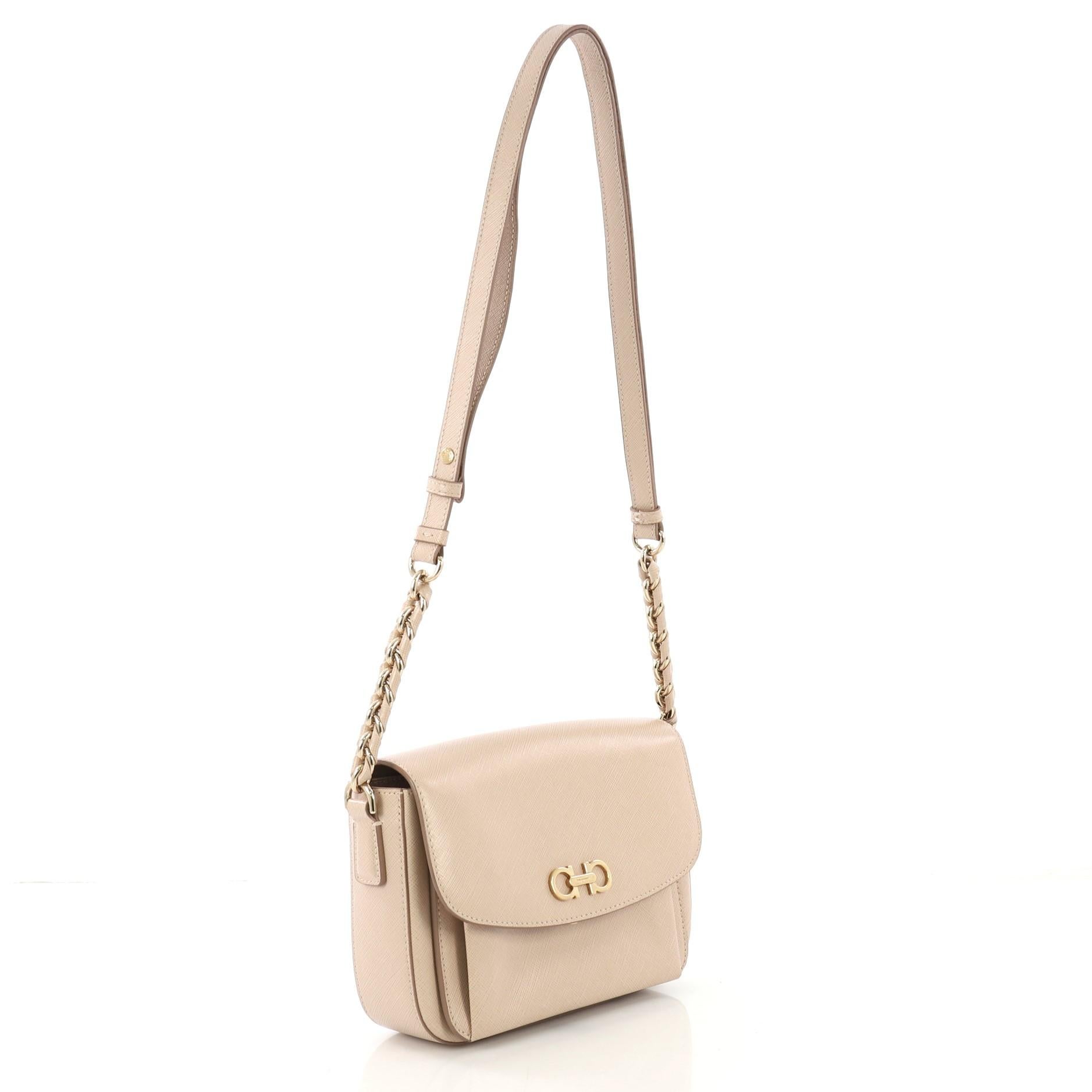 This Salvatore Ferragamo Sandrine Shoulder Bag Saffiano Leather Small, crafted in beige saffiano leather, features an adjustable leather strap, Gancini logo on its flap, and gold-tone hardware. Its hidden clasp closure opens to a brown satin