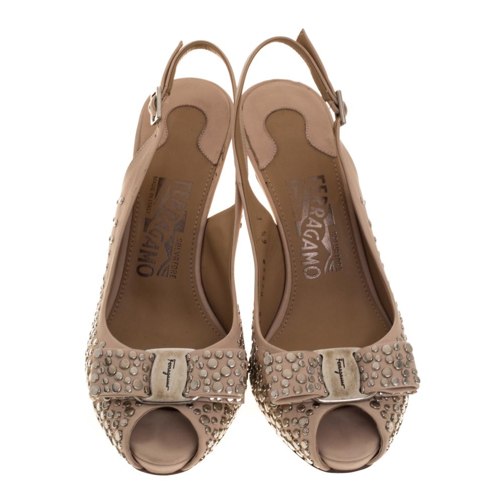 These magnificent sandals from Salvatore Ferragamo are set on concealed platforms and 10 cm heels. They have been crafted from beige studded leather and styled with peep-toes, the signature Vara bows on the uppers, and buckle slingbacks. They are
