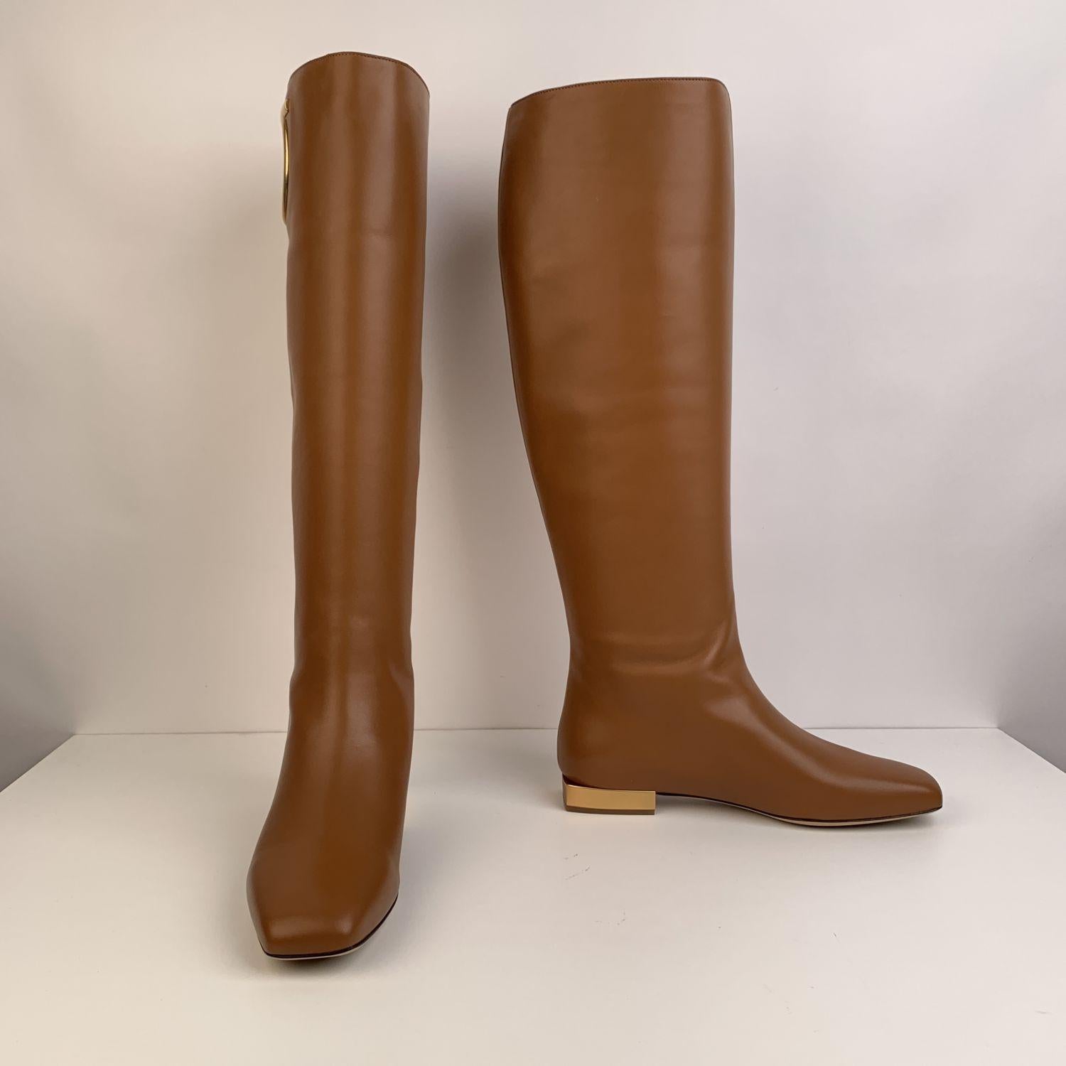 Stunning Salvatore Ferragamo Avio 10 Knee-High Flat Boots. Crafted in tan calf leather, they feature square toe, pull-on style and cut-out Gancino detail on the top. Detailed with gold-tone heels. Leather sole. Heels Height: 1 inch - 2,6 cm. Made in