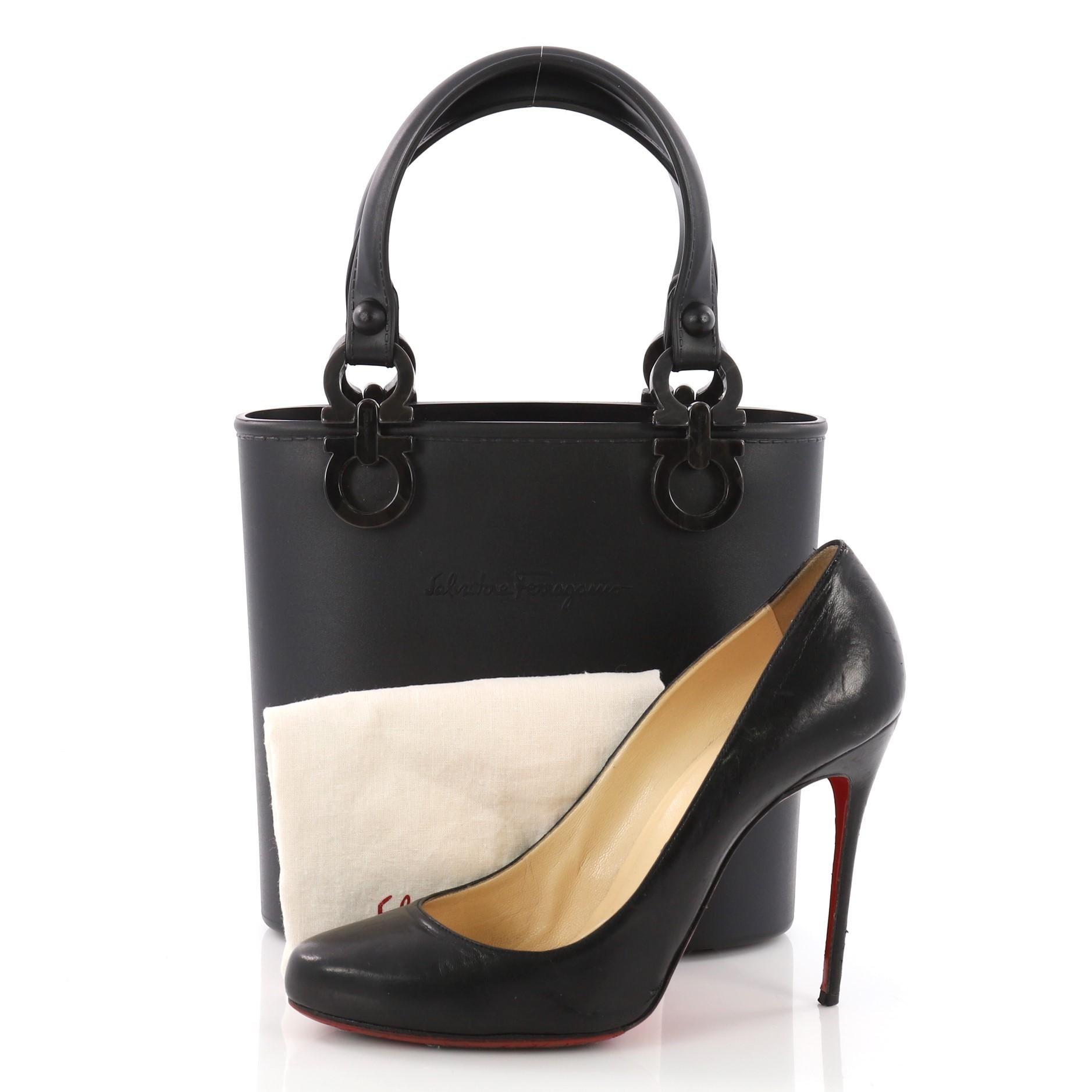 This Salvatore Ferragamo Vintage Gancini Top Handle Bag Rubber Small, crafted from black rubber, features dual flat handles, Gancini accents, and multicolored and silver hardware-tone hardware. It opens to a black rubber interior. **Note: Shoe
