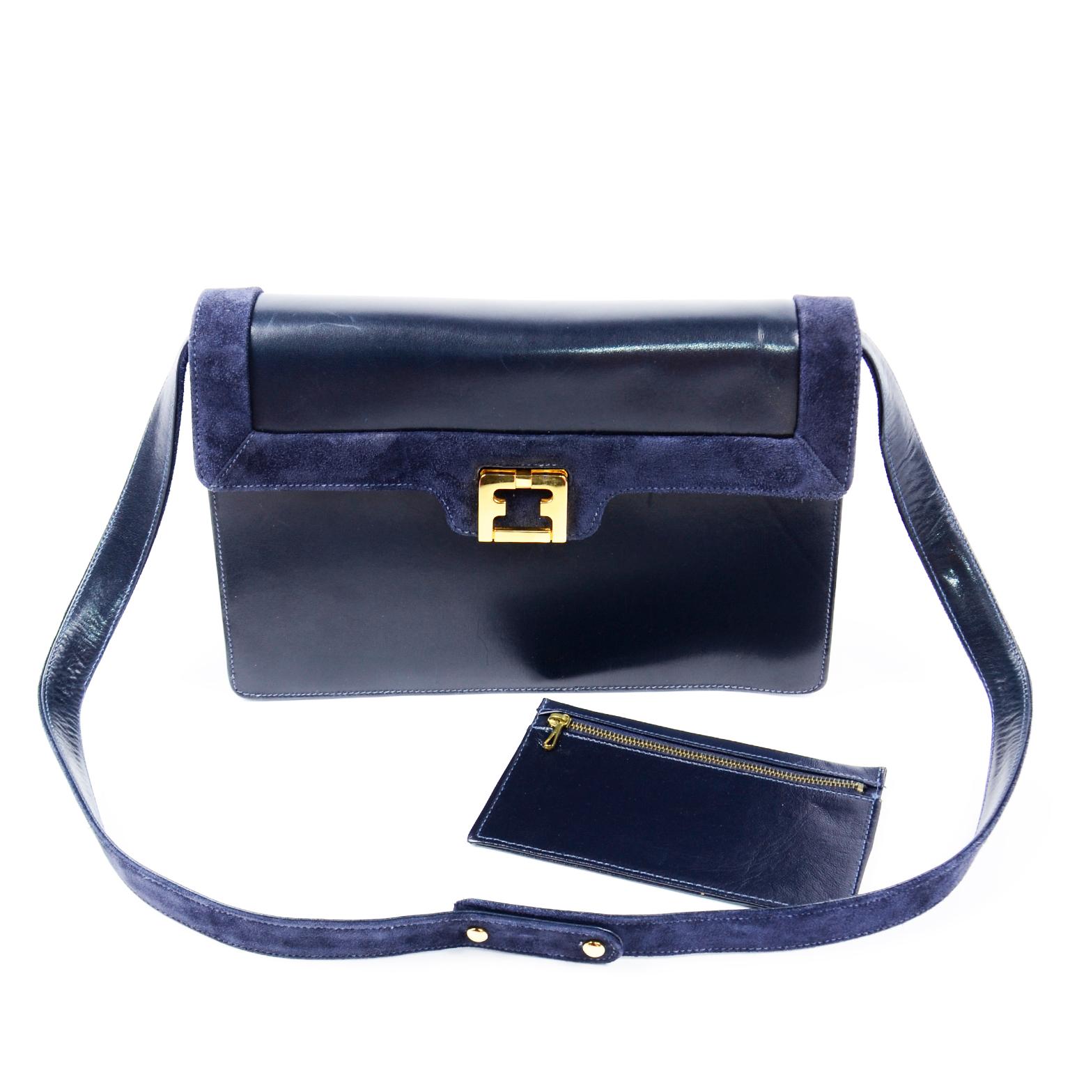 This is a lovely vintage navy blue leather Salvatore Ferragamo handbag with  blue suede trim around the edges of the flap extending to the back and a removable, adjustable suede strap with snaps. We love the pretty gold metal folding clasp! The bag