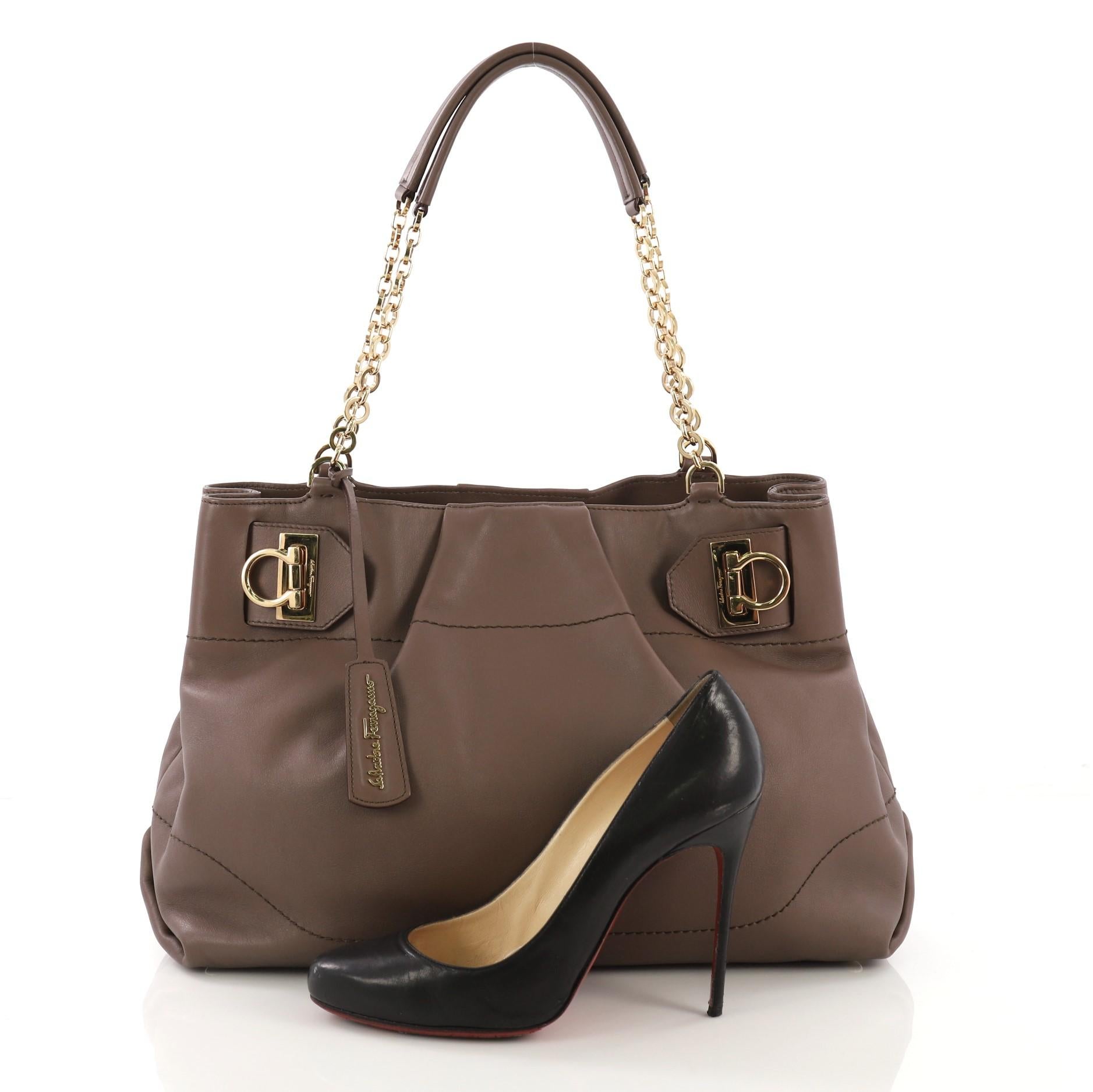 This Salvatore Ferragamo W Chain Tote Leather Large, crafted in taupe leather, features dual chain straps with leather pad, signature polished gold Gancini clasps for a secure closure, protective base studs, and gold-tone hardware. Its brown