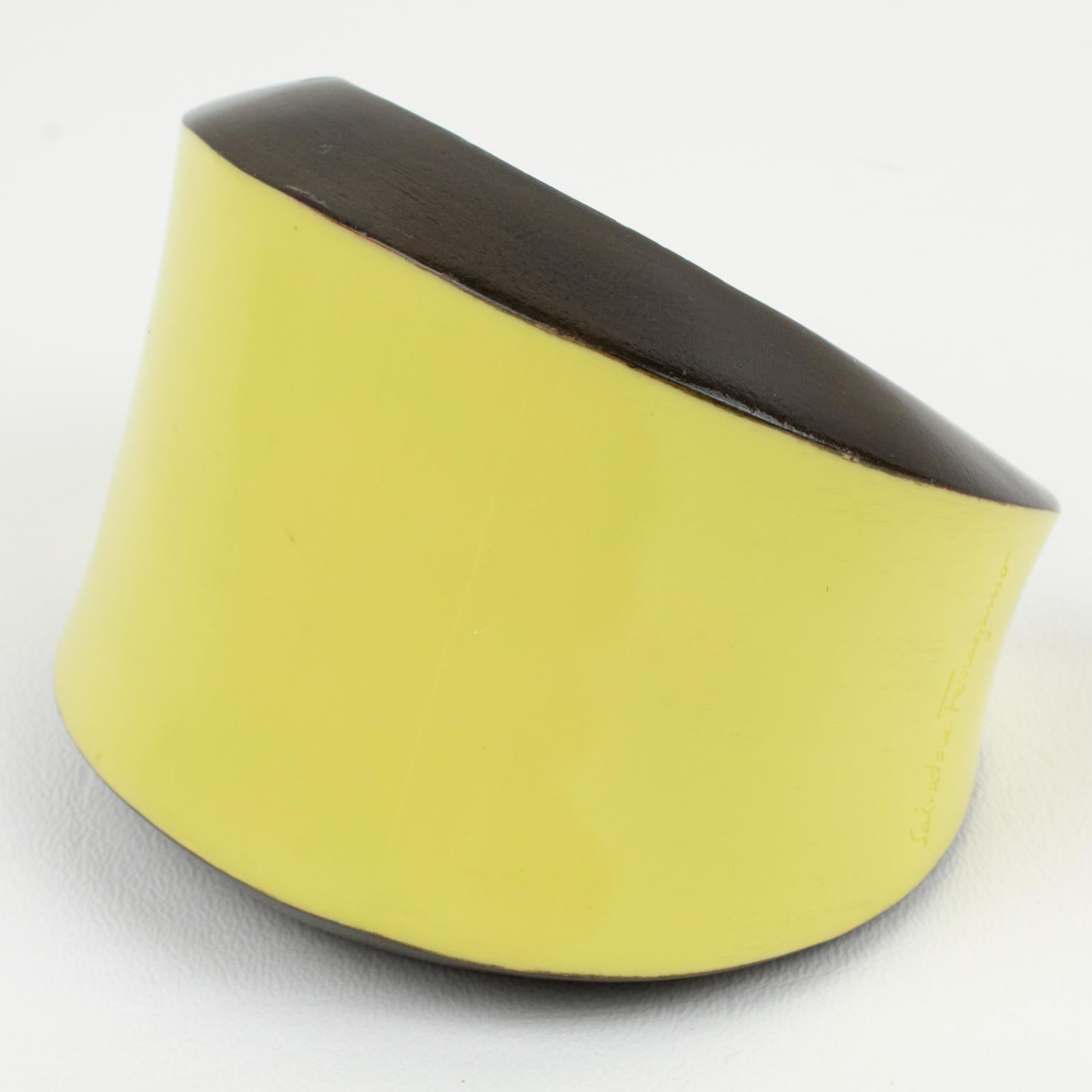 This stunning Salvatore Ferragamo, Italy, bracelet bangle features a massive, geometric, chunky cuff shape, built on carved wood with enamel in pale butter yellow and bittersweet toffee brown colors. The cuff is engraved with a 