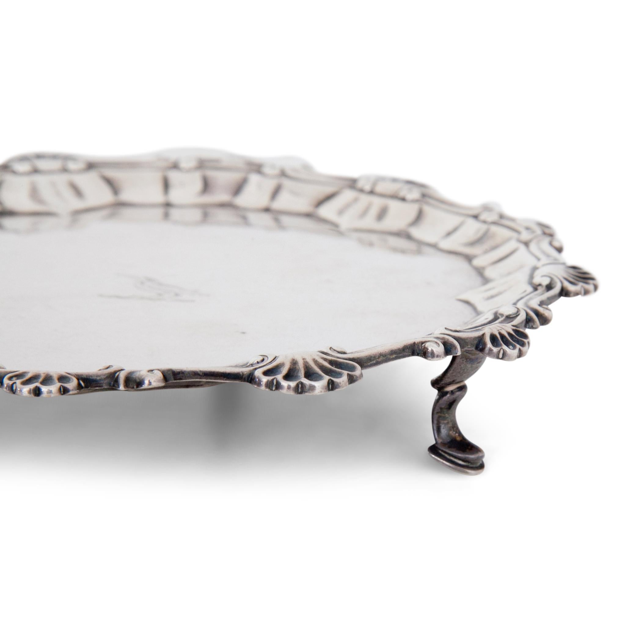 Small silver Salver standing on three feet, the rim of the plate is decorated with shells and rocailles and the well shows a bird. At the bottom Maker’s mark by Ebenezer Coker, London and date letter I for 1764. Measurement: 2.5 x Ø17.