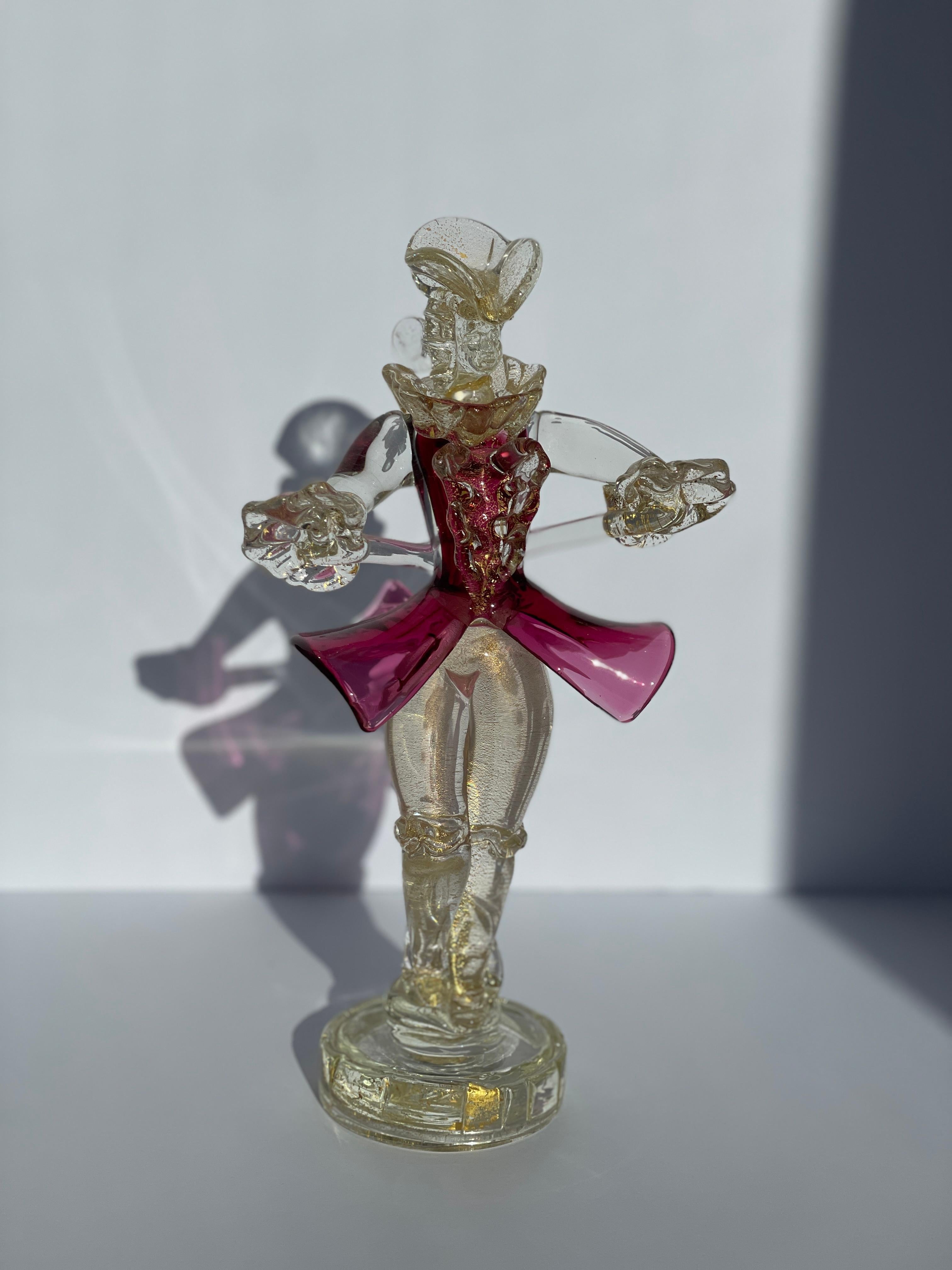 Esta figurita de cristal de Murano de Salviati, bellamente detallada y con la etiqueta original del fabricante, es una cautivadora reproducción del estilo clásico del siglo XVII, fabricada en Italia hacia 1960. La figura, que se alza con gracia