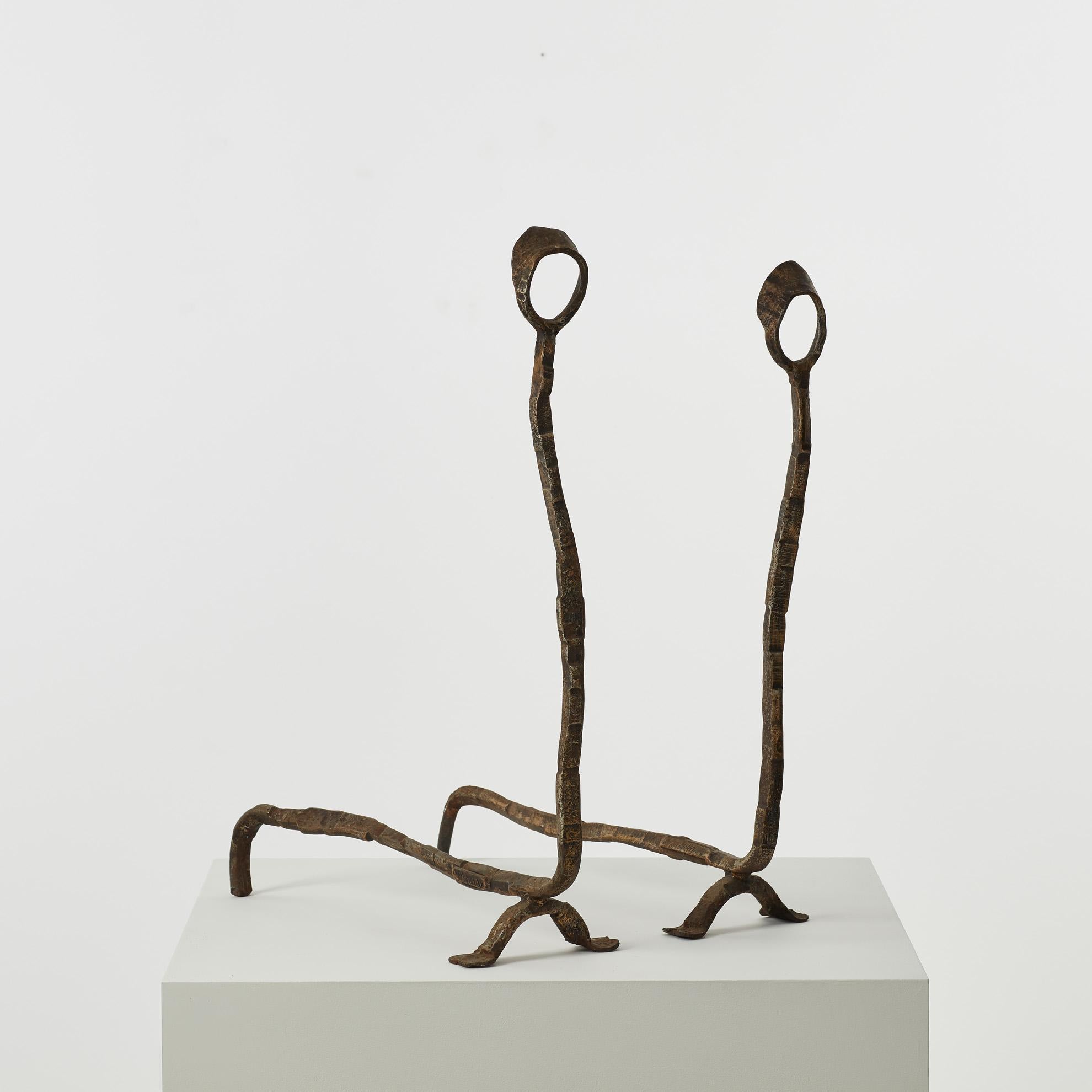 Estos altos soportes de hierro para chimenea están acabados con un detalle decorativo en forma de lazo, que recuerda a dos dientes de león al viento. 

Los morillos están en buen estado vintage, presentan la firma del artista y una pátina fiel a su