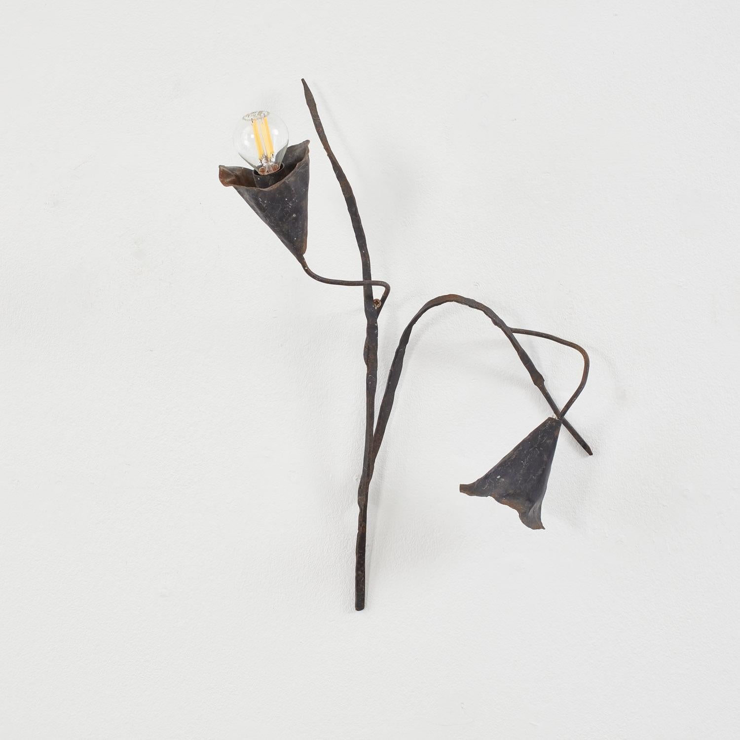 Diese schmiedeeiserne Wandleuchte hat die Form eines zarten, blühenden Stängels mit anmutig geschwungenen Linien und Calla-Lilien-Schirmen. Eine Blüte umschließt die Zwiebel, während eine andere elegant nach unten hängt und so die organische