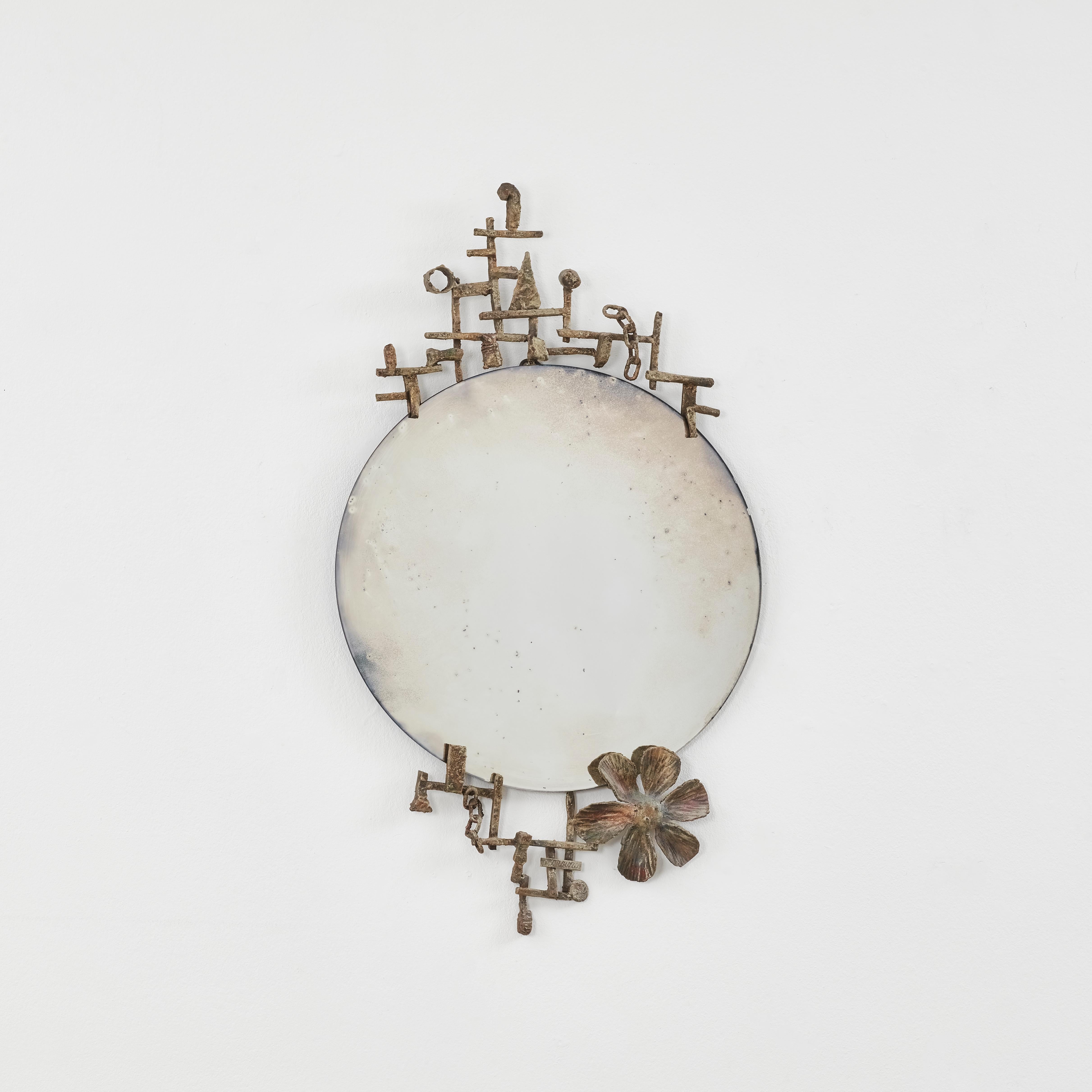 Lines of iron lattice to form a geometric frame around the Forged Mirror I. Within this grid, shapes and motifs gather: a flower, chains, triangles and circles, making it one of Marsura’s more playful and experimental works.

This piece is in good