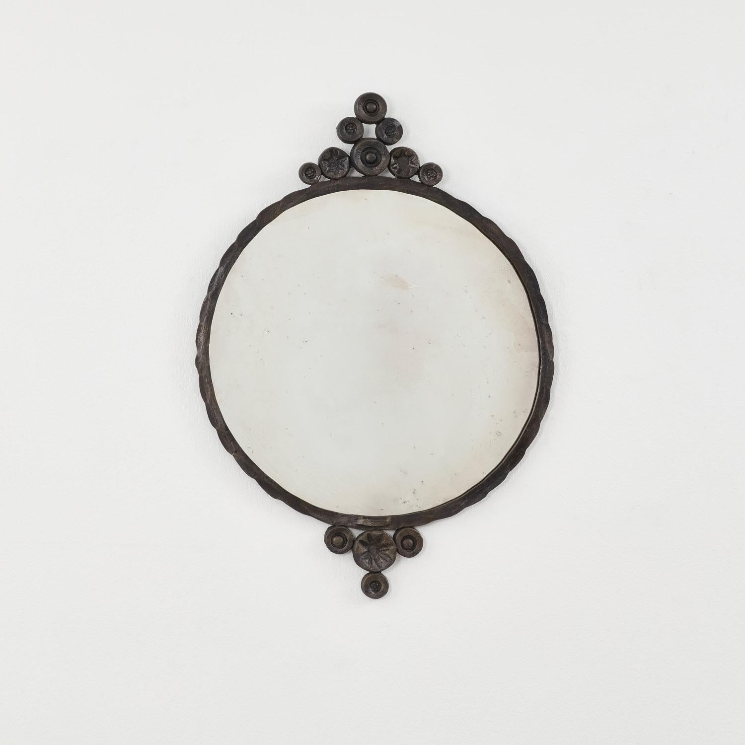 Circles of iron, some marked with pointed-star makings, cluster at the top and bottom of this large round iron mirror. Their arrangement forms a soft ogee at each end, lending the piece a balanced symmetry. 

The iron frame features patination true