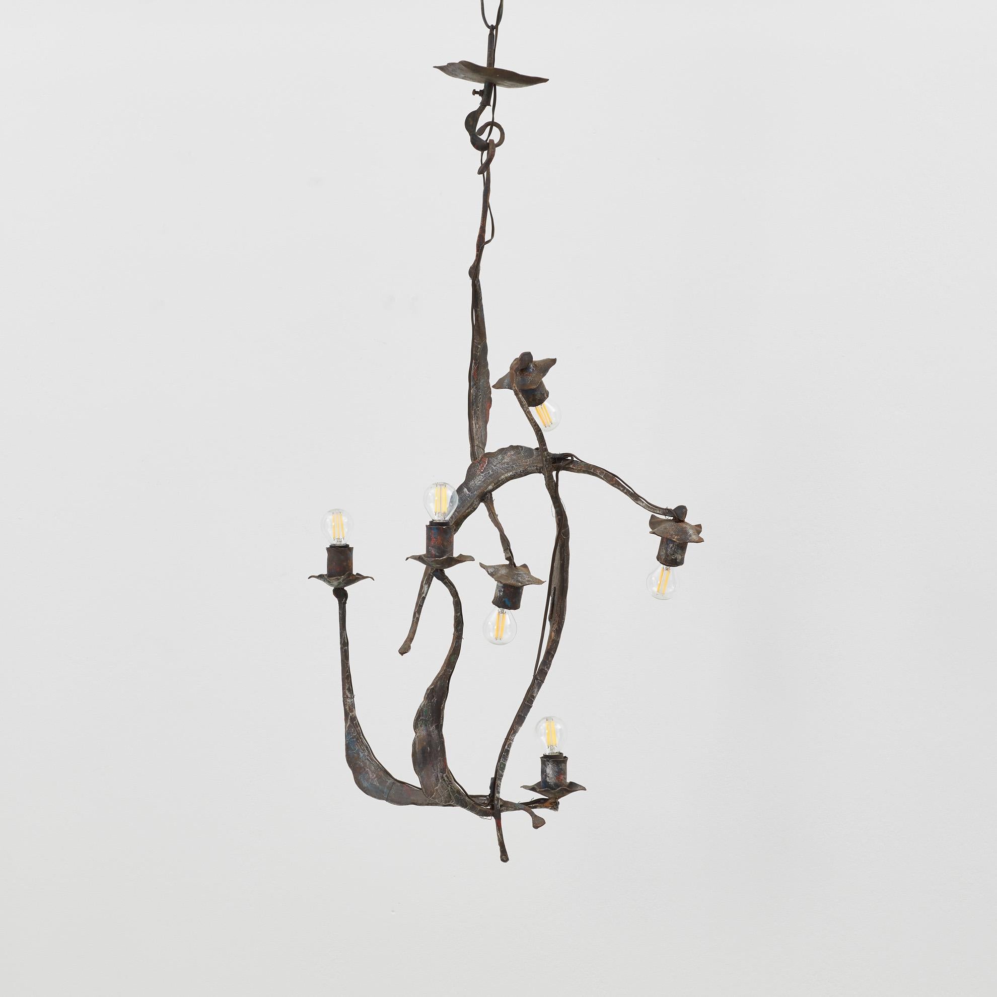 La lámpara de araña Forme III se despliega en una cascada de ramas de hierro, cada una de las cuales sostiene una bombilla que brilla suavemente. Delicadamente equilibrada, la pieza recuerda el crecimiento botánico sigiloso congelado en el