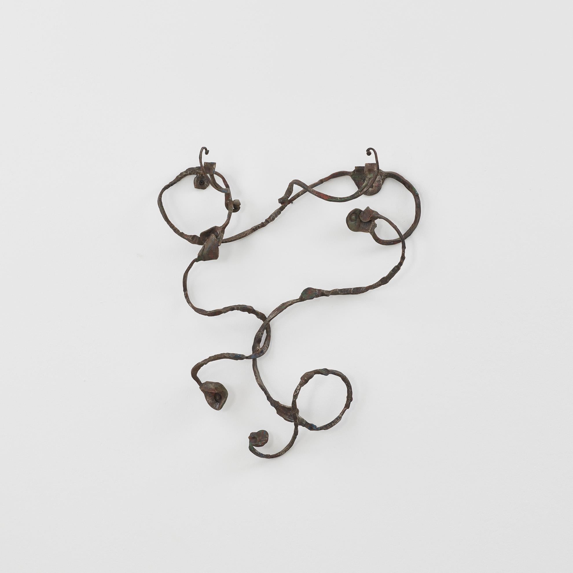 Der Garderobenhaken von Intrecciati ist ein Fragment aus lebendigem Metall, das sich an der Wand ausbreitet. Wie eine kalligrafische Kritzelei verweben sich die gewundenen Stränge in einem organischen Rhythmus, unterbrochen von gewundenen Haken, die