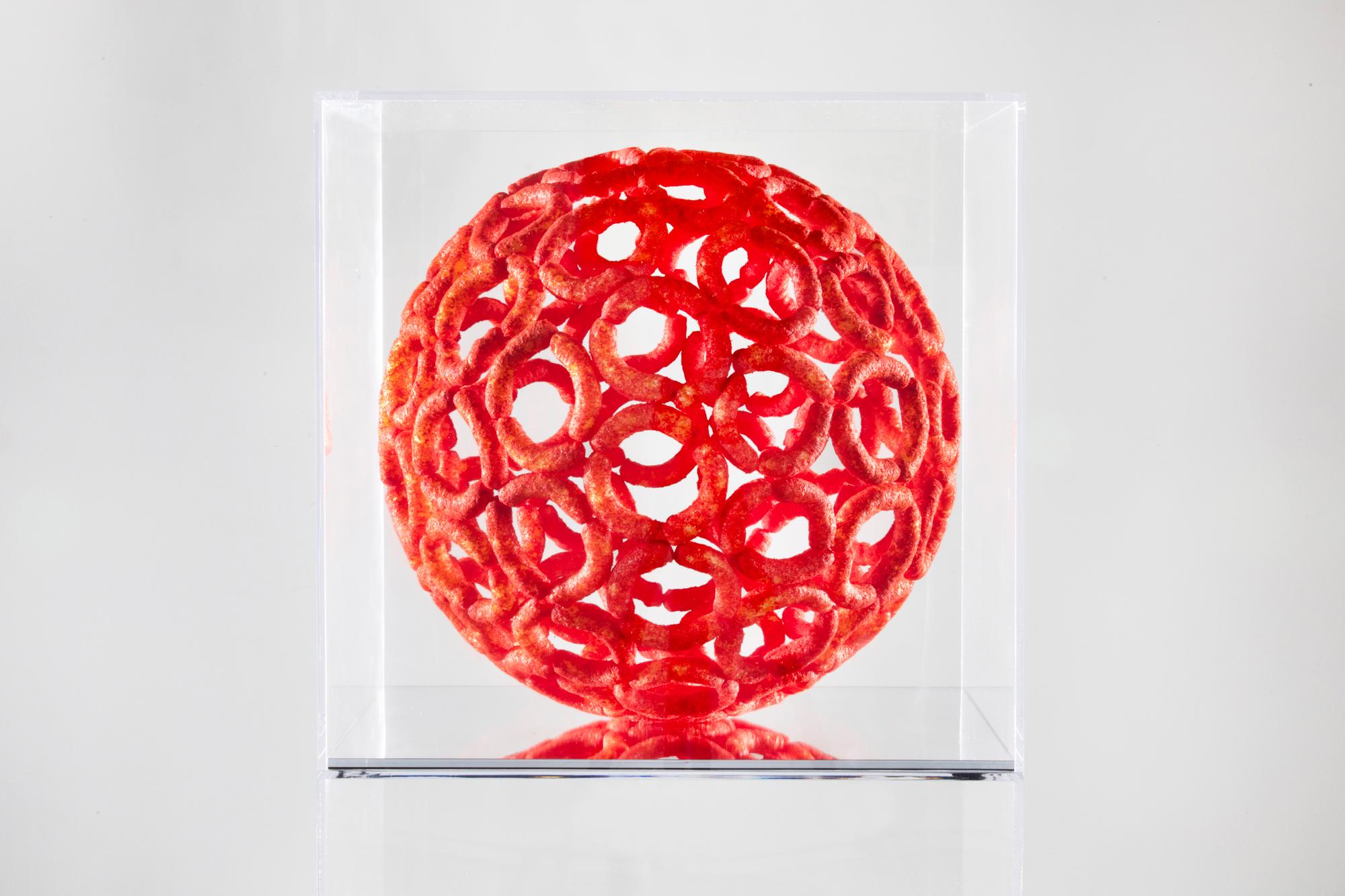 Scultura geometrica realizzata con Flamin' Hot Cheetos Puffs e adesivo dall'artista di Los Angeles Sam Keller. Viene fornito con una teca in plexiglass personalizzata che misura 18 x 18 x 18 pollici. Questo pezzo è stato presentato nella mostra