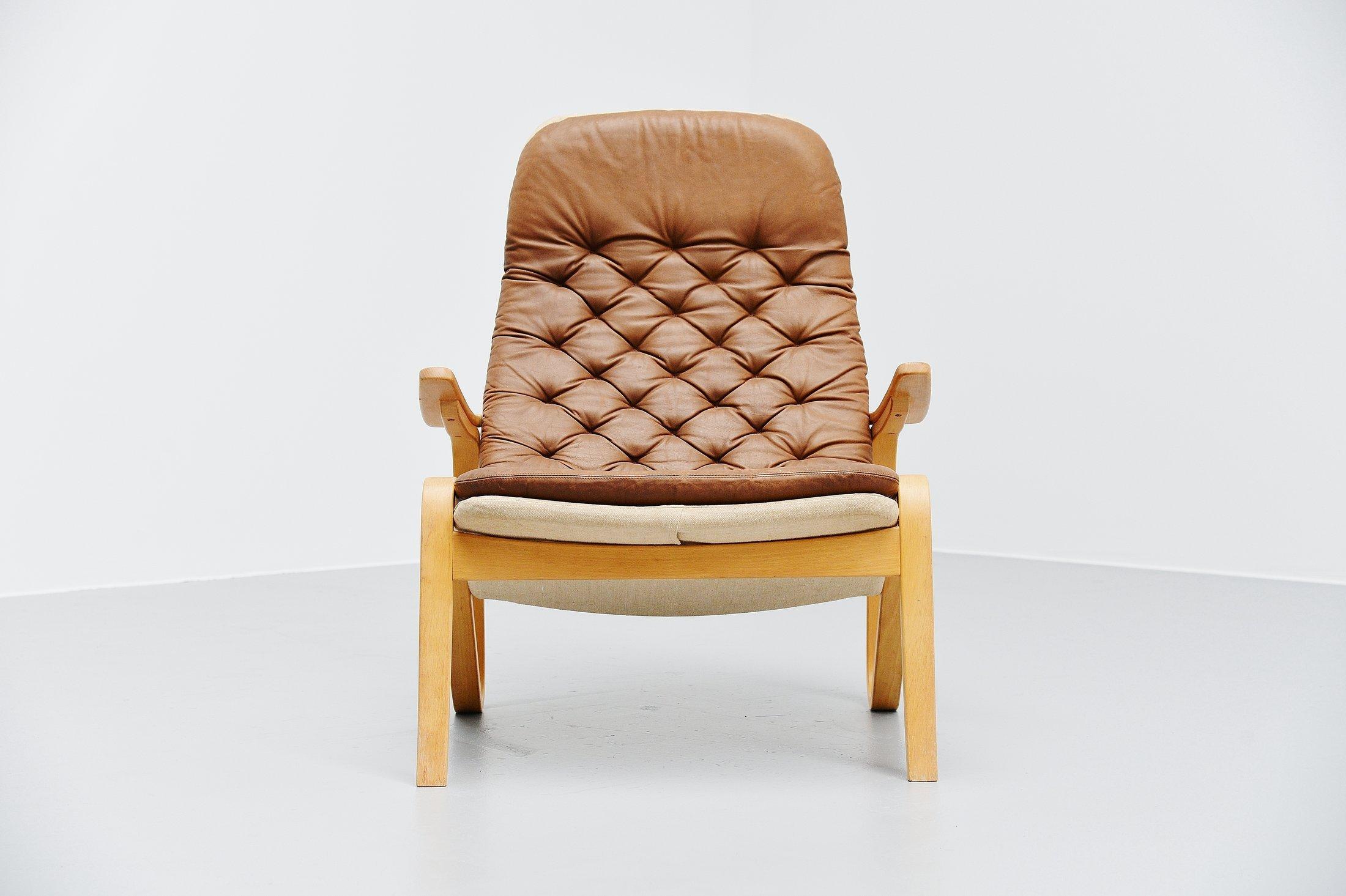 Very nice ‘Metro’ lounge chair designed by Sam Larsson and manufactured by DUX, Sweden 1970. The chair has a birch plywood frame and canvas cover, with natural brown leather tufted seating cushion. The chair is in very nice original condition and