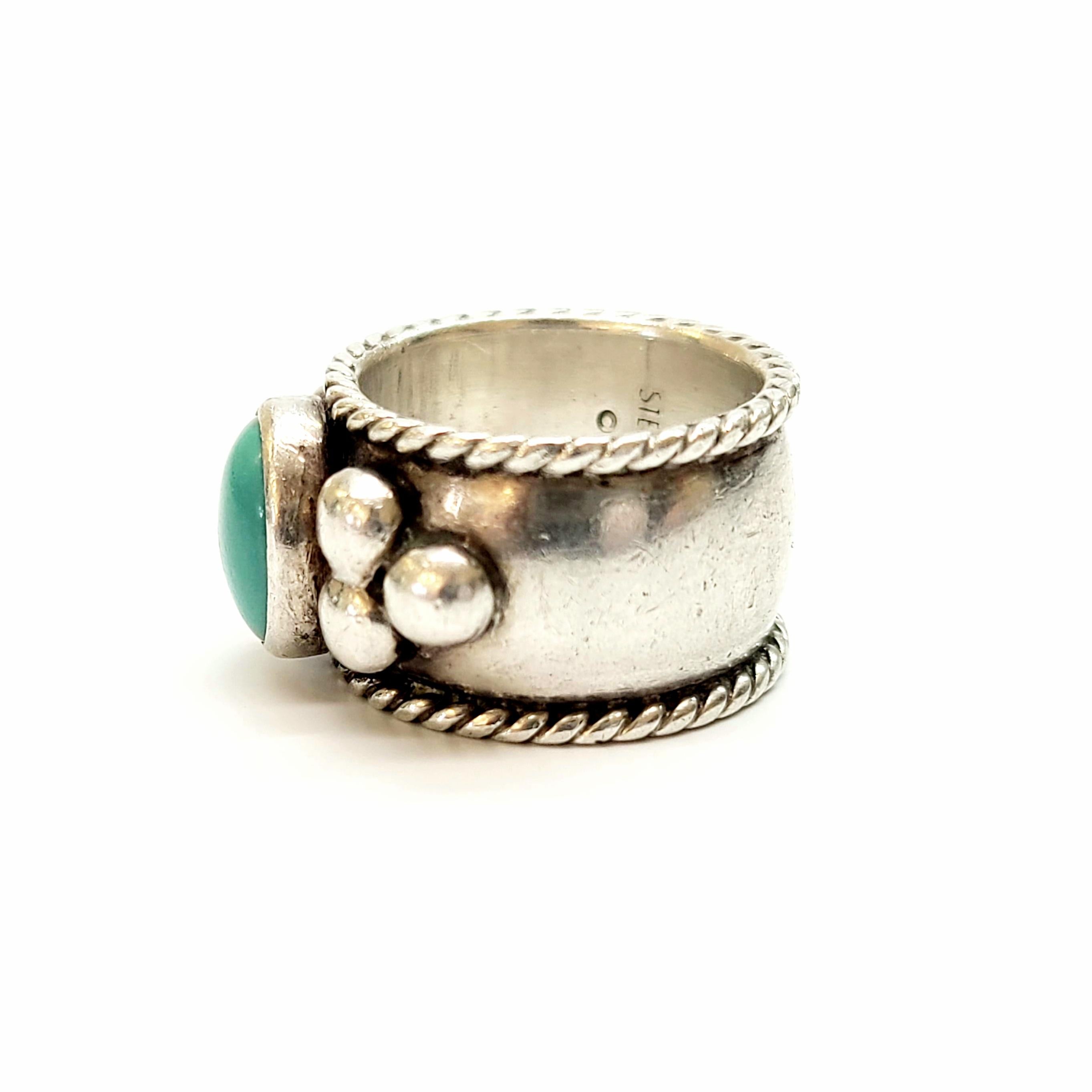 Sterling silver cigar band and turquoise ring by Santo Domingo Pueblo artisan, Sam Lovato.

Size 5

This piece features a bezel set oval turquoise stone, flanked on each side by a cluster of three silver beads, on a rope edged band.

Measures approx