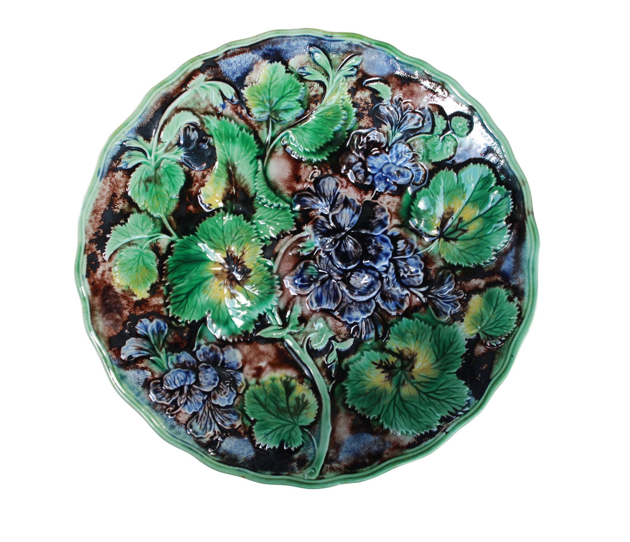 Samuel Alcock & Co. Majolica purple glazed geraniums plate, English, circa 1860, molded with purple glazed geranium blossoms, stems and leaves glazed in green, yellow and brown, reserved on a faux bois ground within a shaped green glazed