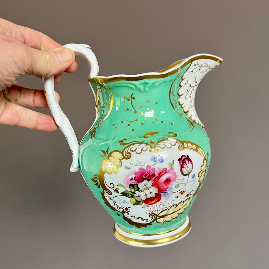 A cream or water jug / pitcher with knobbed twig handle and moulded foliage under the beak, decorated in a pale green ground with a finely painted landscape on one side and rich flowers on the other, set in a gilt and pale yellow foliage