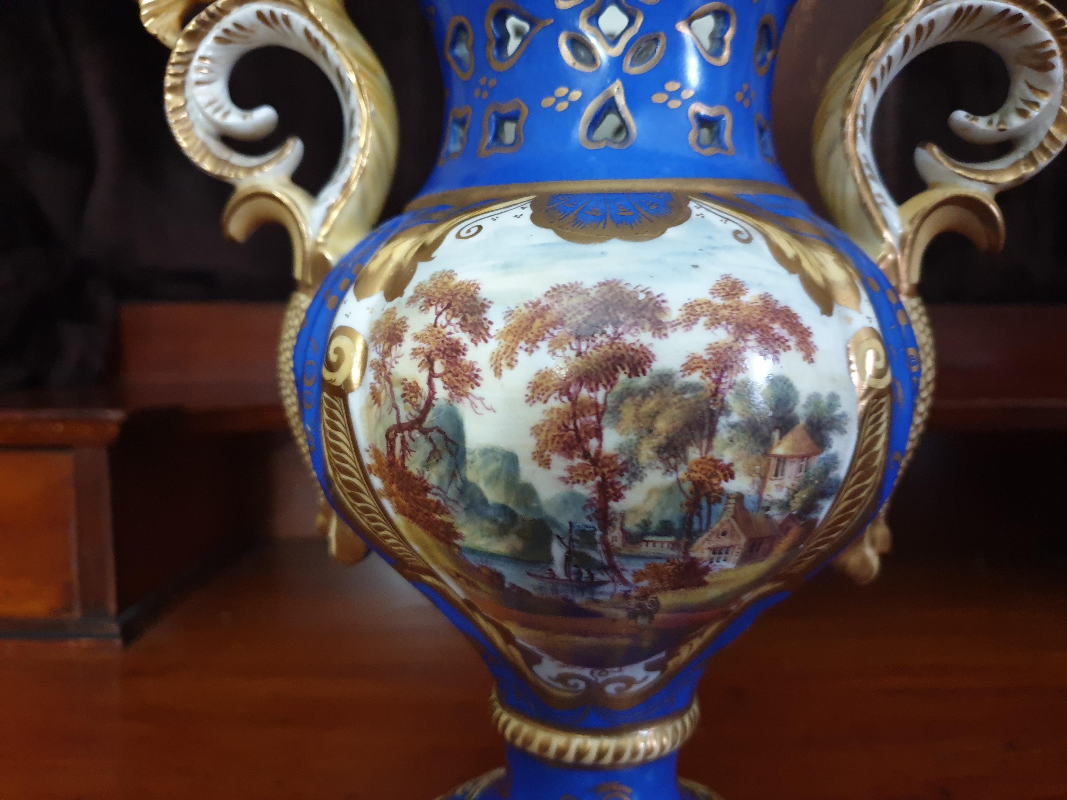 This Samuel Alcock griffin vase is decorated in Sèvres celeste blue color with a gorgeous hand painted natural landscape scene on one side and a lavish gilt detail on the other. A bulbous body with a fat perforated neck in the finest Rococo style