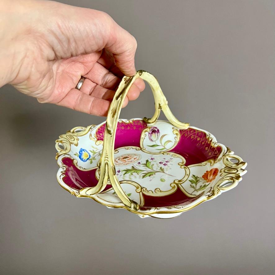 A maroon ground basket in Rococo Revival style with pierced pale yellow ends, a twig handle and five flower reserves with single flowers.

Pattern 2/5610
Year: ca 1835
Size: 22.5cm (8.75”) long, 13cm (5”) tall
Condition:  handle has been repaired,