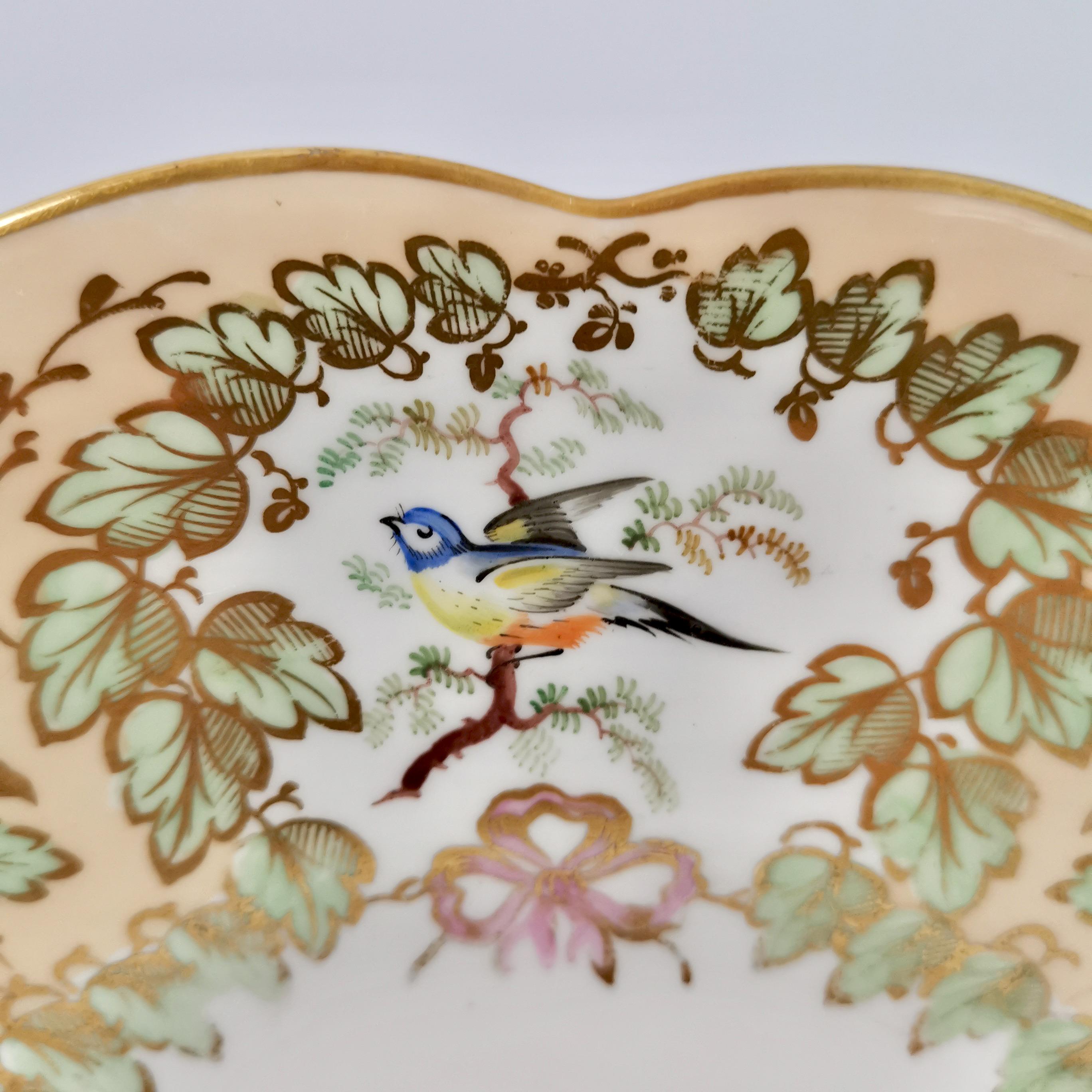 This is a beautiful cake plate made by Samuel Alcock around the year 1845. The plate is decorated in a peach ground with very fine hand painted birds, foliage and beautiful gilding. 

Samuel Alcock was one of the many potters in Staffordshire such