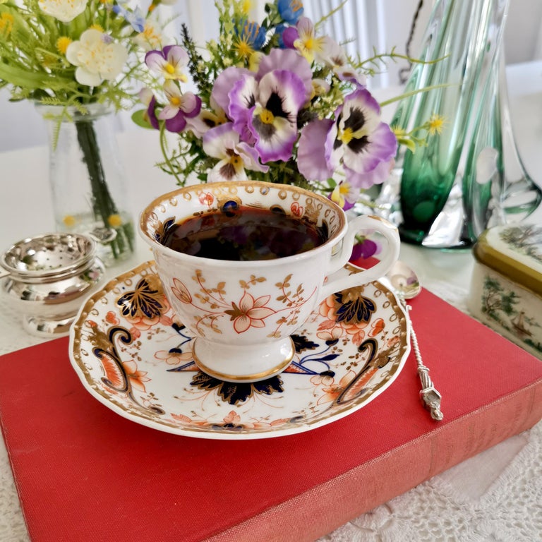 This is a beautiful coffee cup and saucer made by Samuel Alcock around 1830, which was the Rococo Revival era. The set is decorated with a bold Imari pattern and has a 