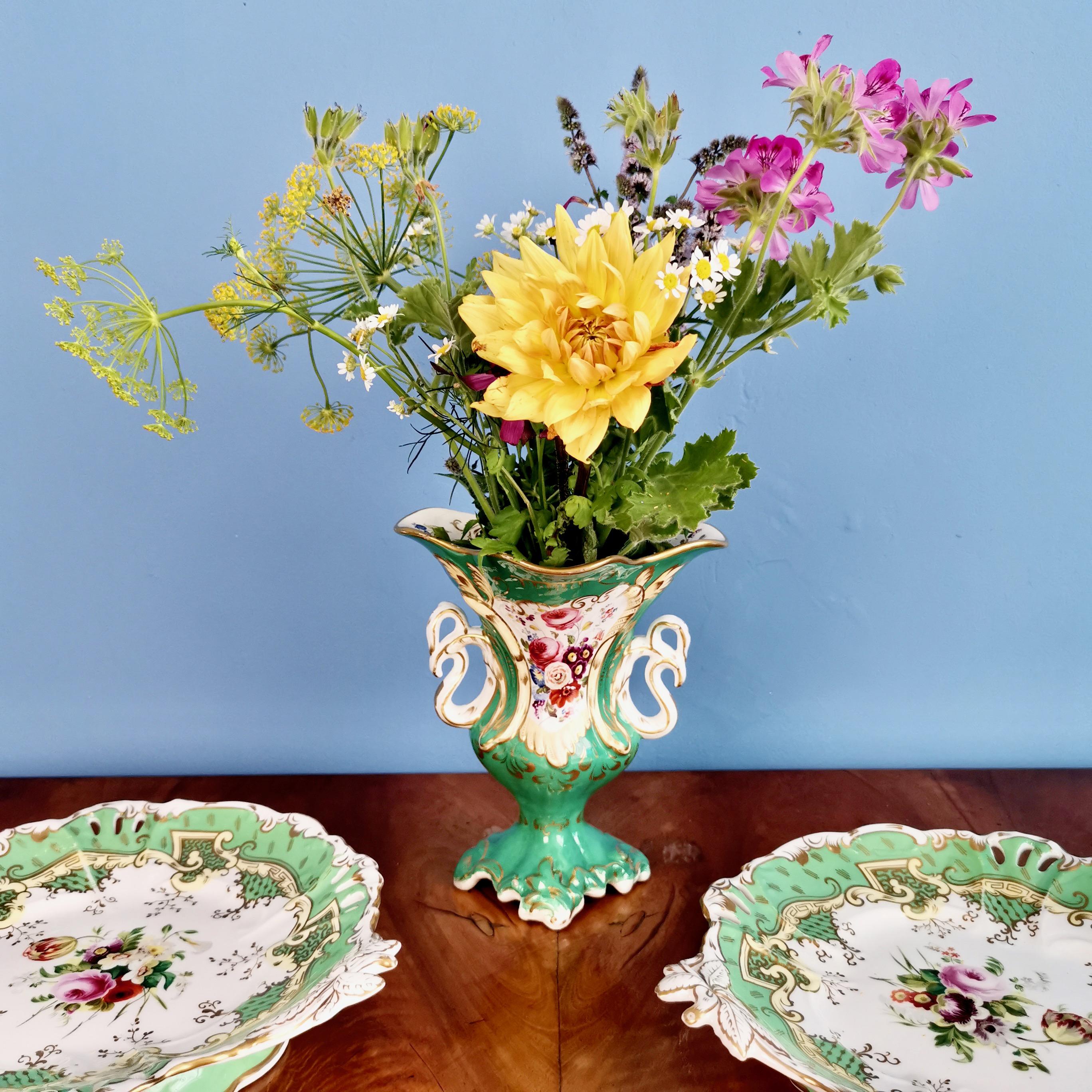 On offer is a beautiful vase made by Samuel Alcock around the year 1840 during the Rococo Revival era. The vase has an emerald green ground and white swan-shaped handles on either side. It is painted with a beautiful landscape on one side and