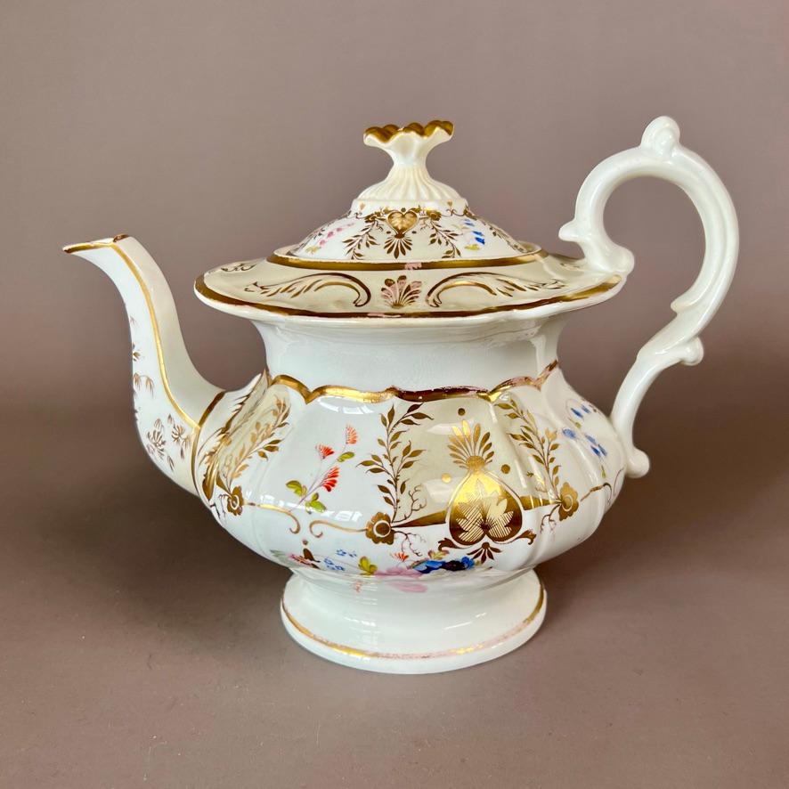 A solitaire tea set consisting of a teapot with cover and a trio consisting of a teacup, a coffee cup and a saucer, in “rustic loop” shape, with beige ground with rich pale yellow and gilt acanthus pattern and beautiful flower posies in the centre