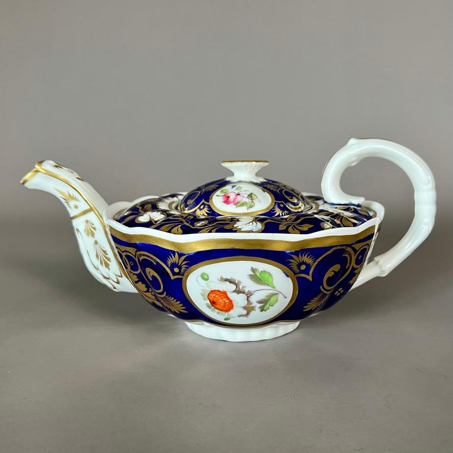 A solitaire tea set consisting of a teapot with cover, a milk jug and a small cup and saucer, in “melted snow” shape, the cup with double drop handle, with deep cobalt blue ground, rich gilt vines and hand painted flower reserves. The teapot and cup