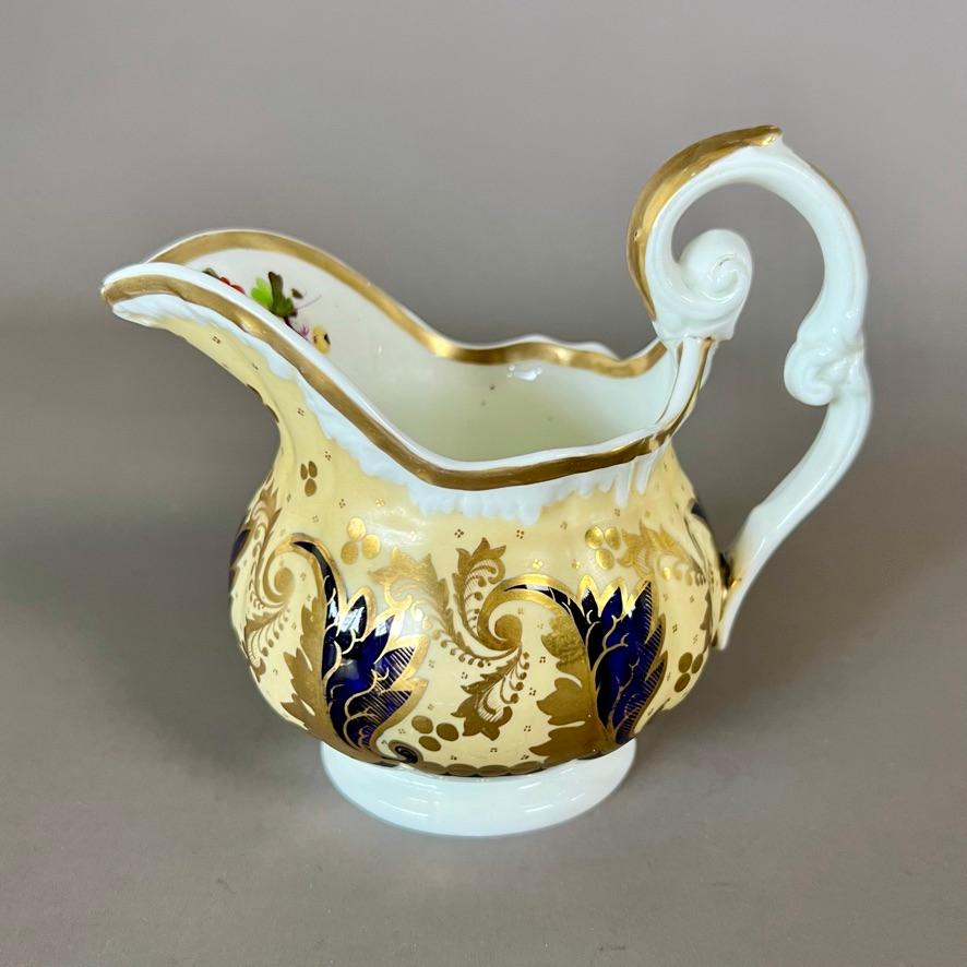 A teacup and saucer with milk jug in the “melted snow” shape with double drop handles, pale yellow ground with rich gilt and cobalt blue acanthus pattern and finely painted flower reserves in centre teacup, saucer and inside the mouth of the milk