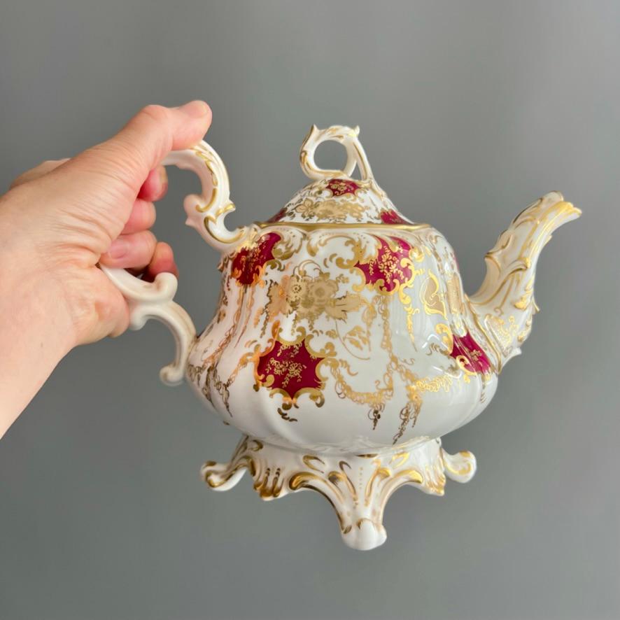 Théière en forme de poire, de style néo-rococo, avec couvercle, pied à volutes et acanthes, bec verseur, fleuron à boucle et poignée, décorés en doré. Cartouches bordeaux, dorures en forme de champignons et feuillage de saule pleureur descendant sur