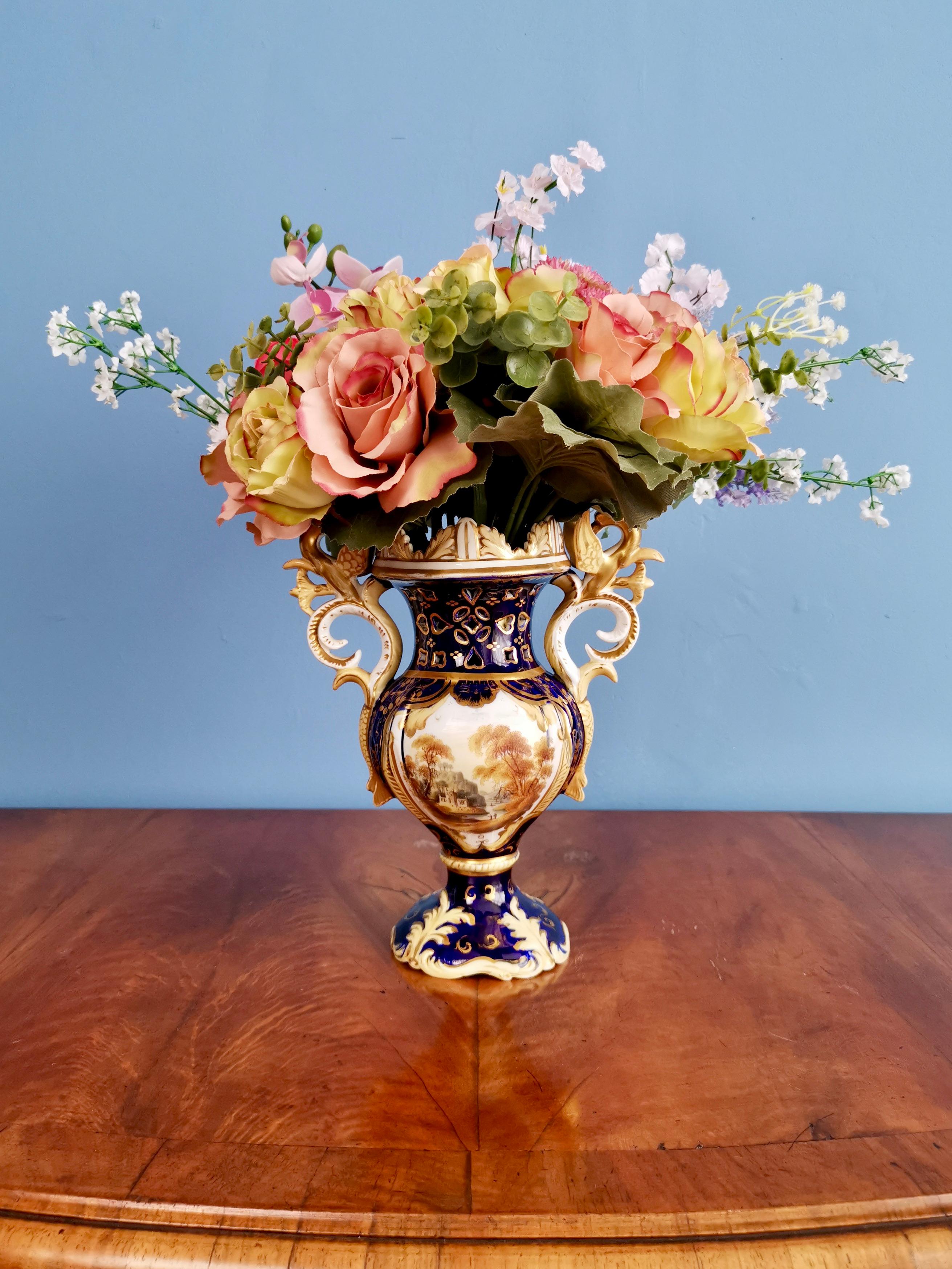 Angeboten wird eine schöne Porzellanvase von Samuel Alcock aus der Zeit des Rokoko-Revivals um 1840. Die Vase hat griffige Henkel, einen kobaltblauen Grund, eine üppige Vergoldung und eine schöne Landschaftsmalerei.

Samuel Alcock war zwischen den