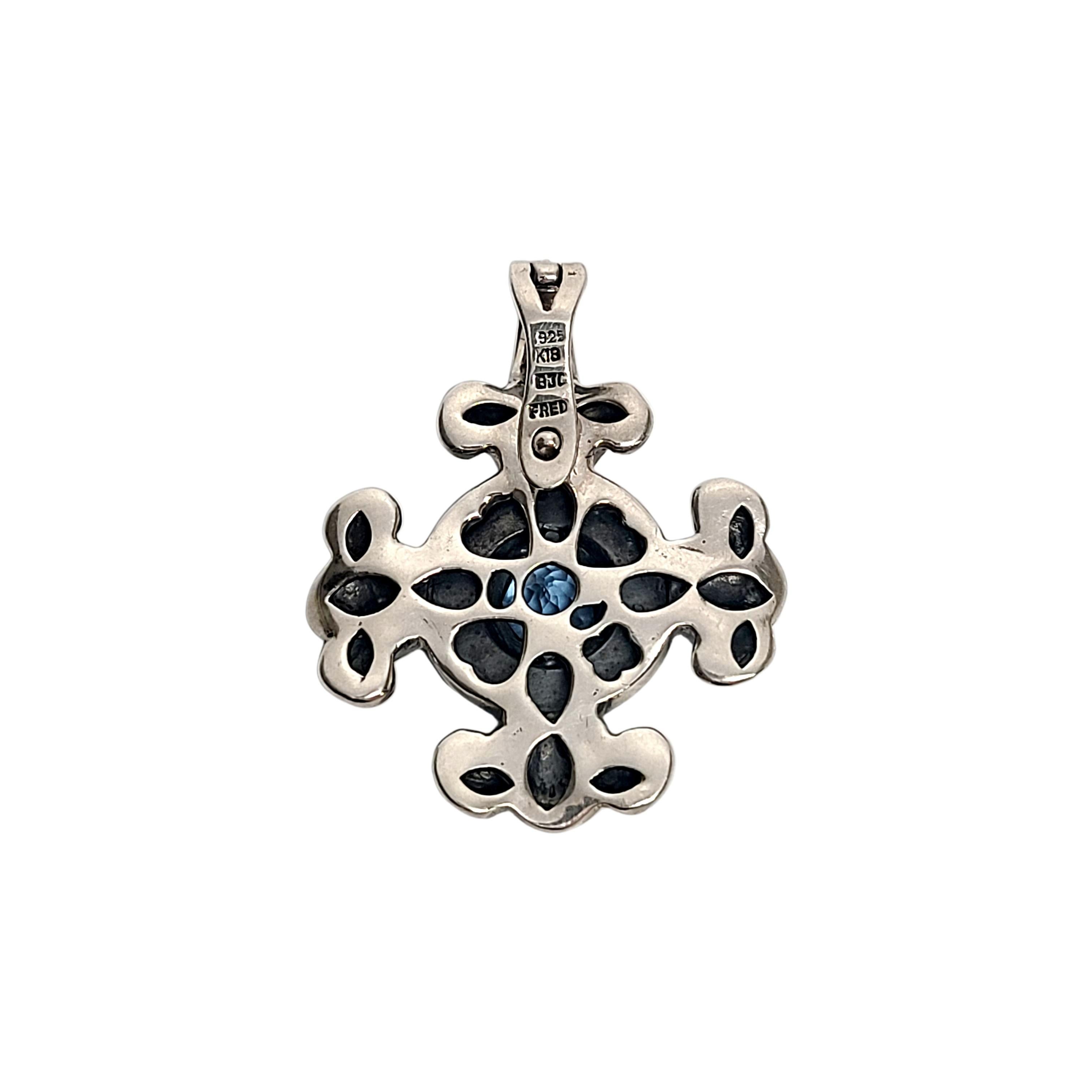 Sterling silver 18K yellow gold accent blue topaz pendant by Samuel Benham BJC Fred.

Round blue topaz stone stone set sterling silver cross shape pendant with yellow gold beaded accents around the stone. Hinged opening bail.

Measures approx 1 