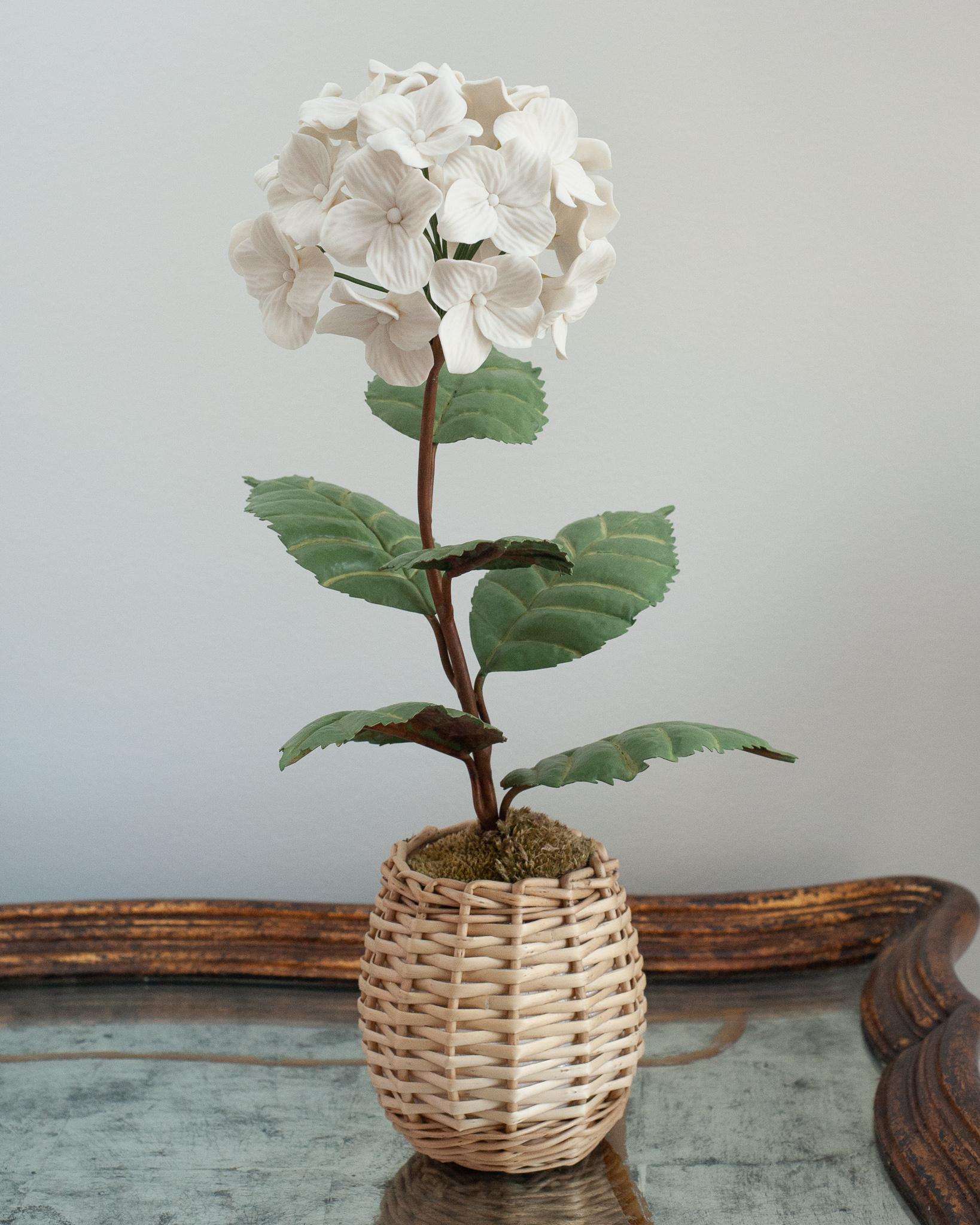 Enhance your table with these delicate porcelain flowers by French artist Samuel Mazy. This white hydrangea is handmade in biscuit porcelain, with handpainted copper leaves and stems, and is placed in a wicker pot. 
An exclusive floral collection
