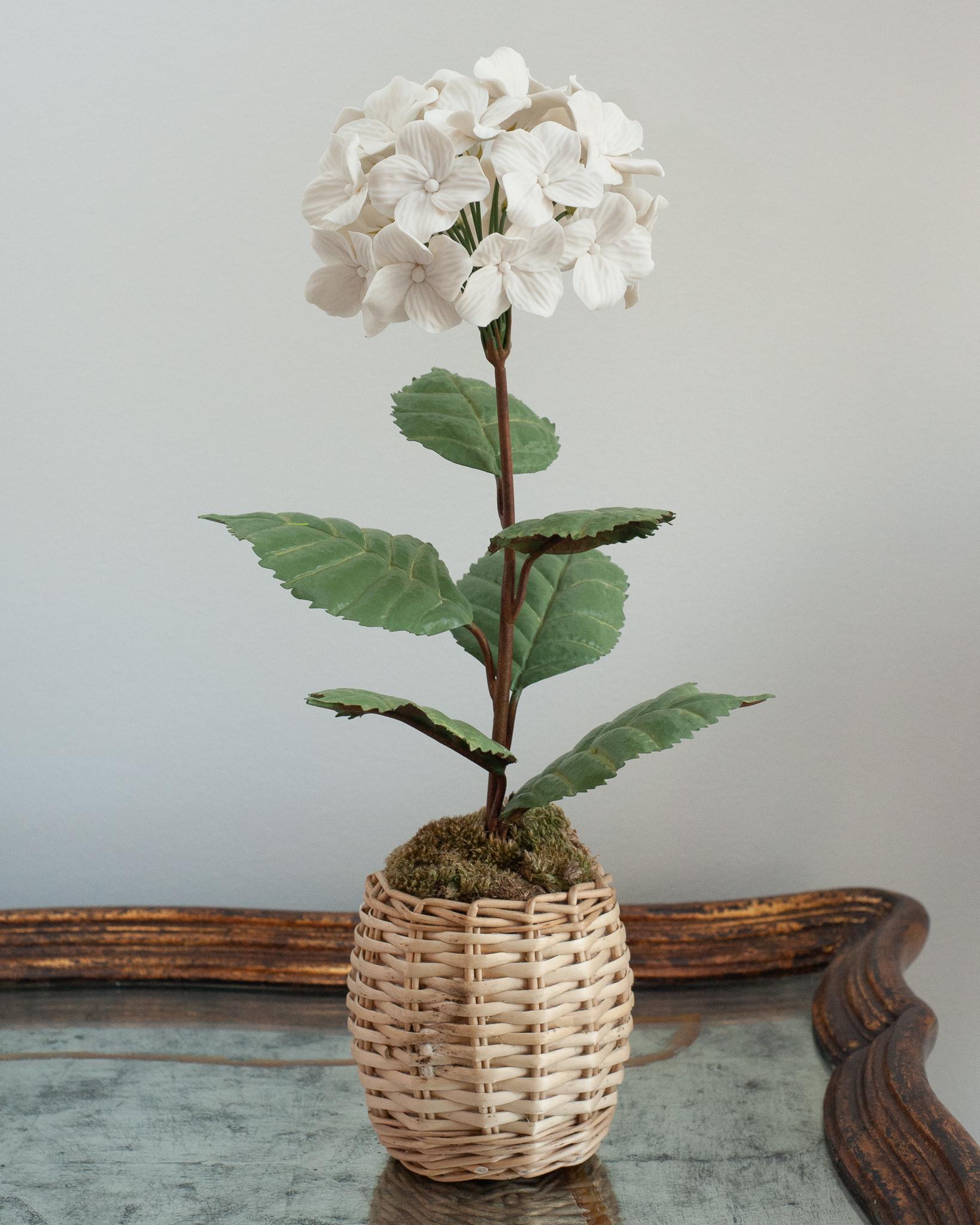 Verschönern Sie Ihren Tisch mit diesen zarten Porzellanblumen des französischen Künstlers Samuel Mazy. Diese weiße Hortensie ist aus Biskuitporzellan handgefertigt, mit handbemalten Kupferblättern und -stängeln, und steht in einem Weidentopf. 
Eine