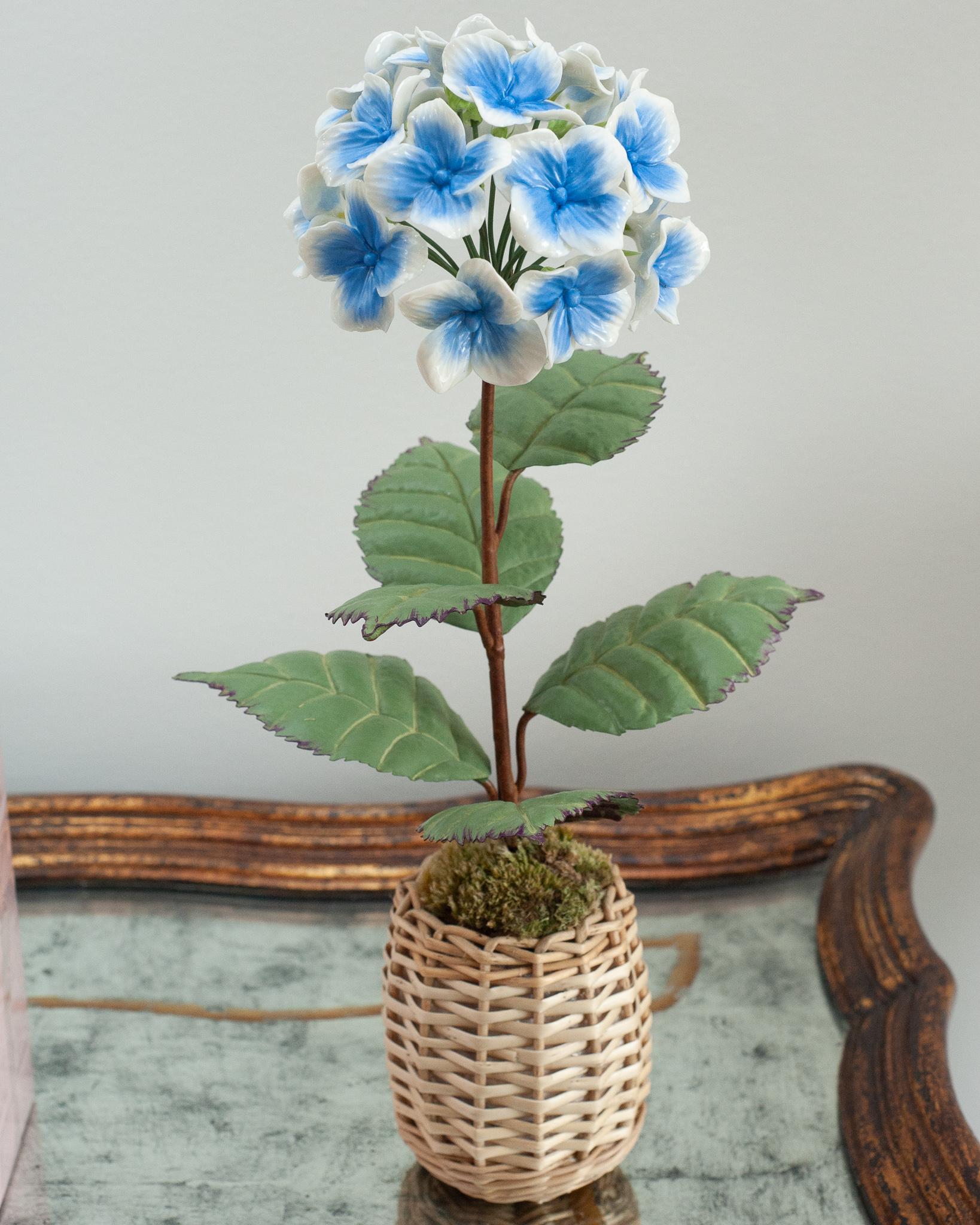 Enhance your table with these delicate porcelain flowers by French artist Samuel Mazy. This blue and white hydrangea is handmade in glazed porcelain, with handpainted copper leaves and stems, and is placed in a wicker pot. 
An exclusive floral