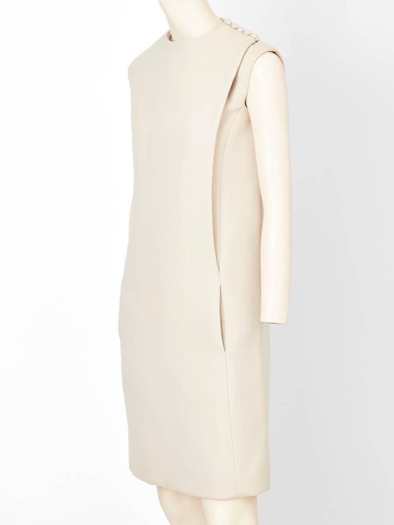 Robe blanche, en gaberdine de laine Samuel Winston, à manches courtes, ligne A, créée par Norman Norell. La robe a des coutures décentrées de chaque côté de la robe avec des fermetures à boutons couvertes à l'épaule.