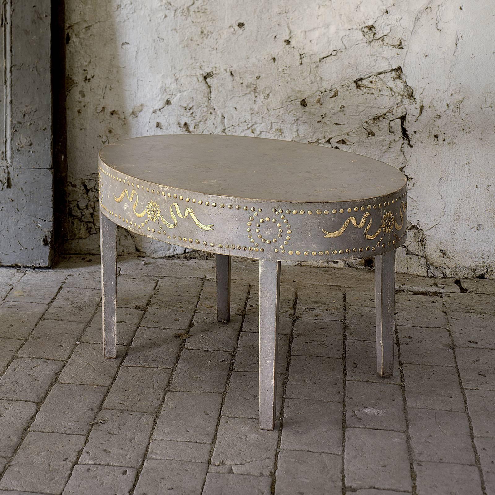 The classic oval shape of this unique table is paired with a light umber color with antiqued finish to create a sophisticated piece that will complement any decor. Crafted of wood, hand painted pale yellow garlands and nail head trims decorate its