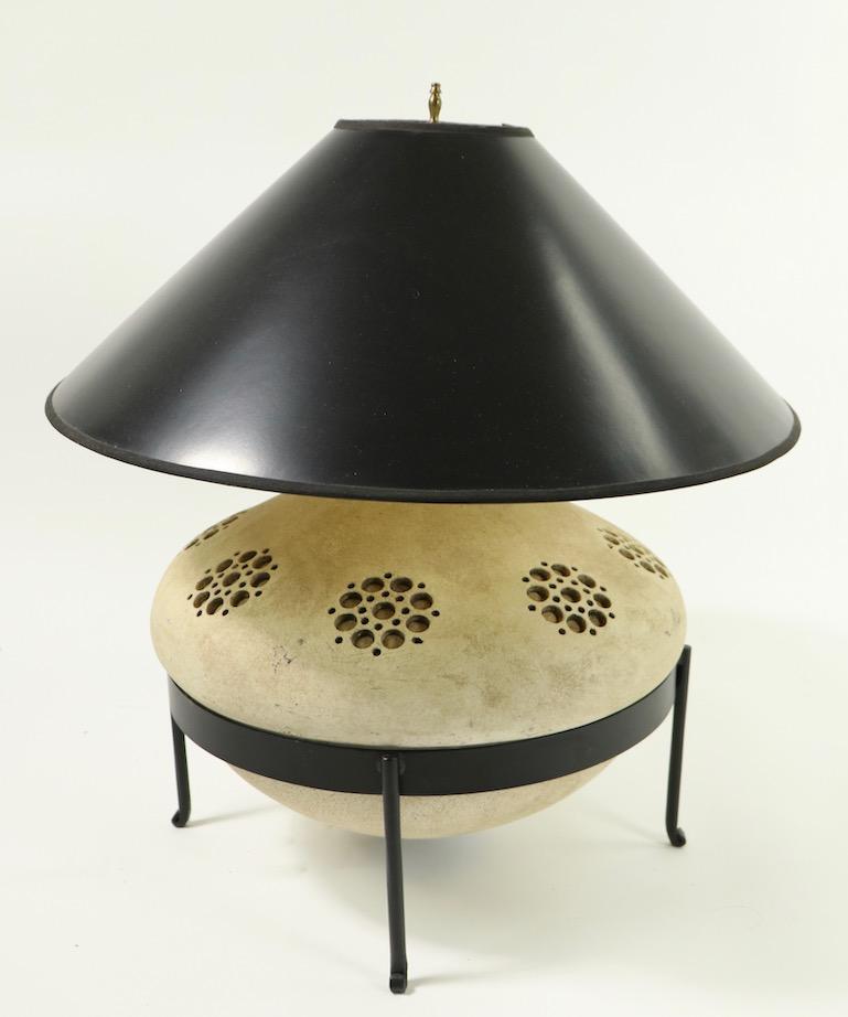 Chic 1970s ceramic lamp in original wrought iron base stand. The large bulbous ceramic lamp base (17 inch diameter) has circular cut away decorative design elements. The lamp is in clean and working condition, it accepts a standard size screw in
