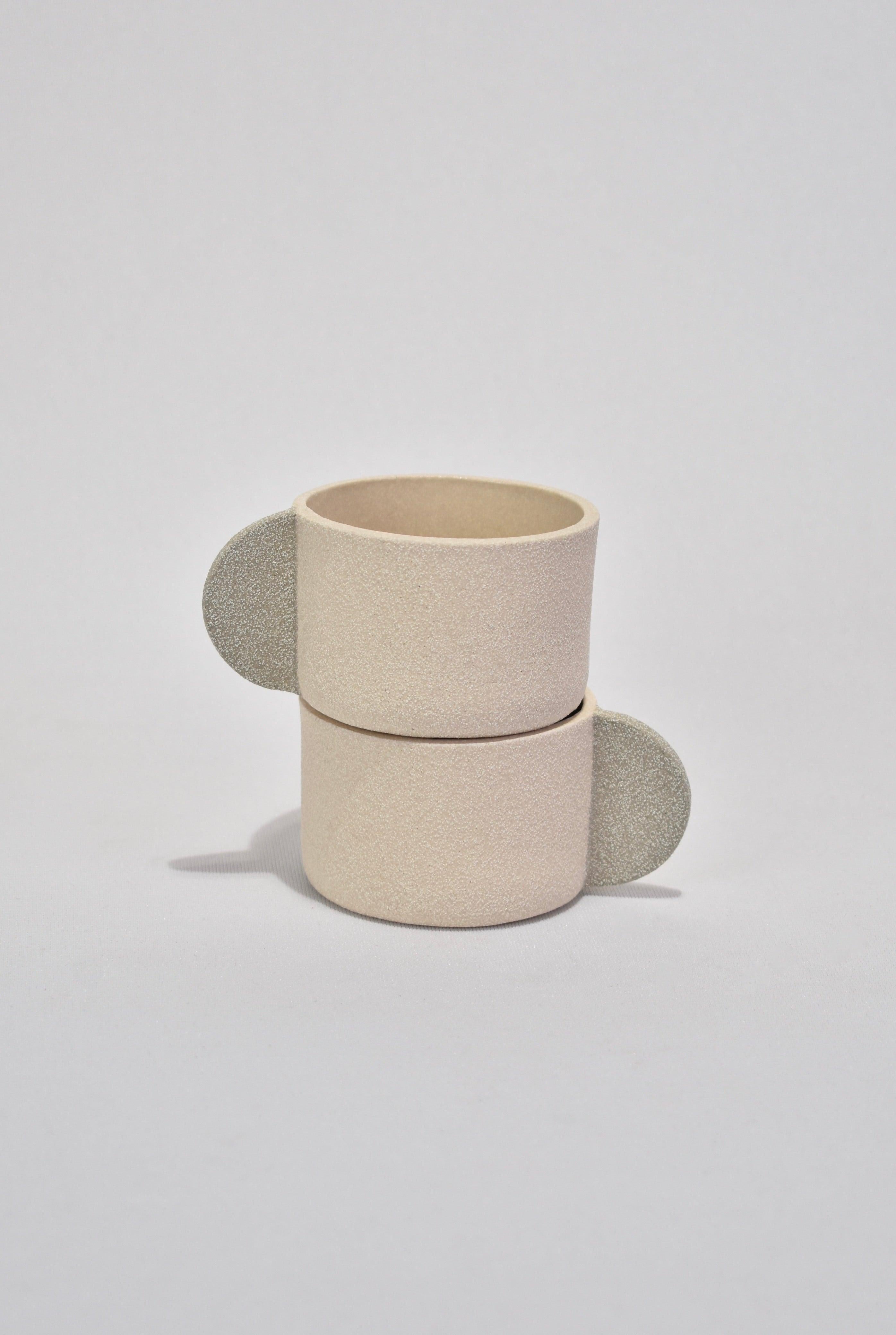 Sand stoneware double espresso set with a textured matte exterior and transparent gloss glaze on the interior. Each cup features a light grey semi-circle handle and BRUTES stamped on base. Set includes two cups.

Handmade in London by Emma de