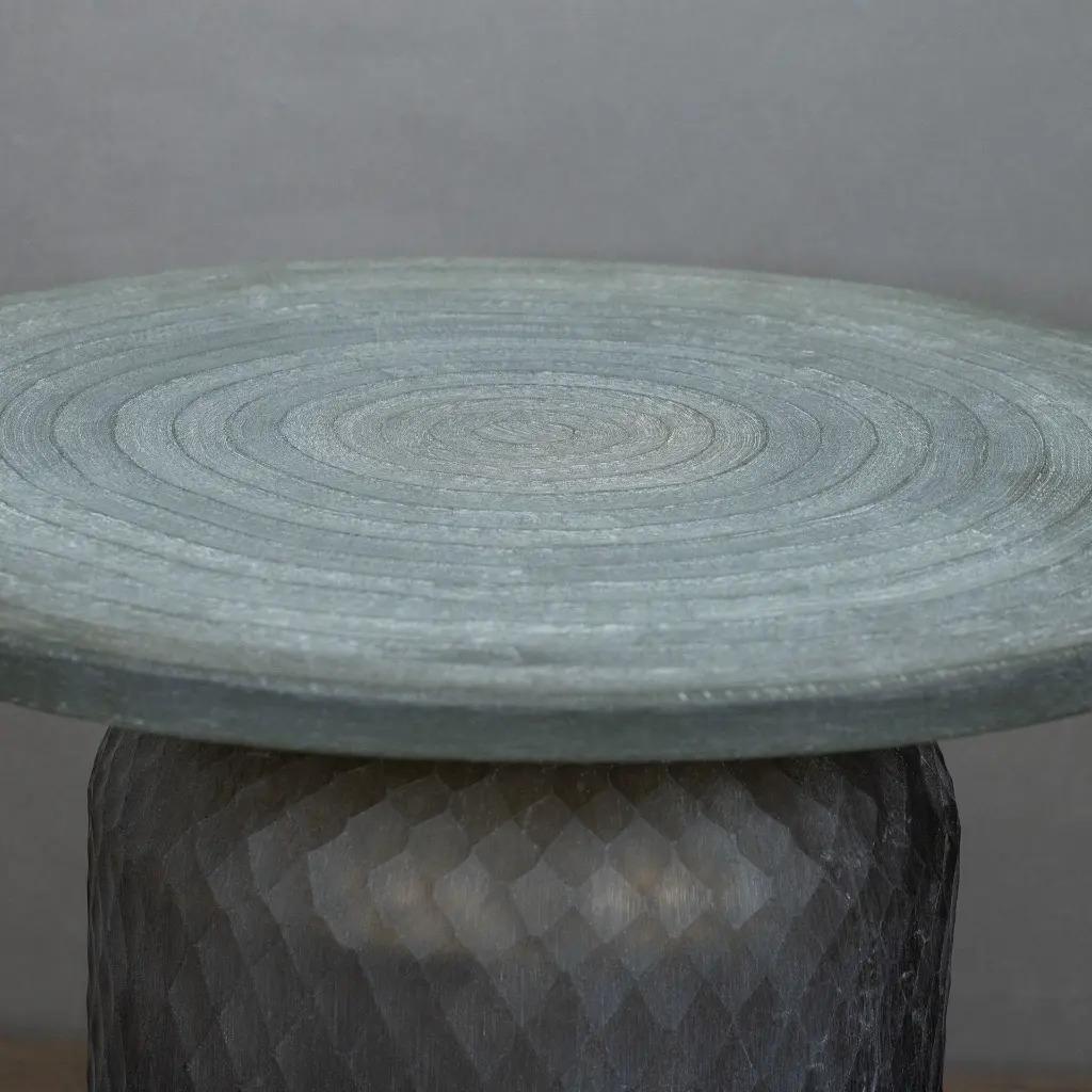 Avec sa forme géométrique audacieuse et sa silhouette sculpturale, cette table en verre s'impose comme une véritable œuvre d'art fonctionnelle. Entièrement fabriquée en verre sablé, elle évoque la texture de la pierre taillée tout en conservant la