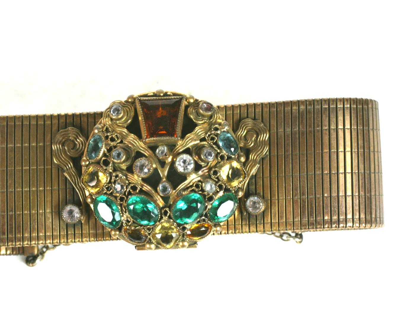 Unusual Sandor Art Deco Compact Bracelet made in the 1930's with a jeweled face. Pastes in emerald, topaz, aqua and citrine are elaborately set onto the face of the compact.
The central motif is set on a flexible, ribbed brass bracelet with