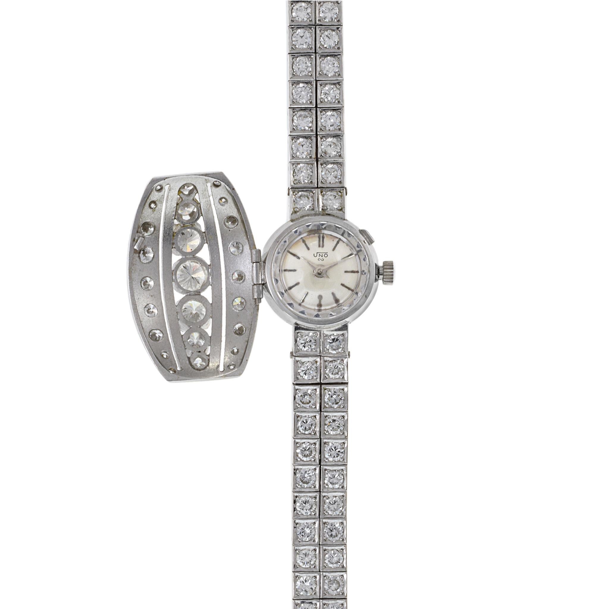 This is a mid century gem a solid 18K white gold Sandoz Uno cocktail watch. This watch is decorated with 8.00CT/F-H color VVS1 and VS diamonds. It features a flip cover over the dial encrusted with seven large diamonds. The actual case of the watch