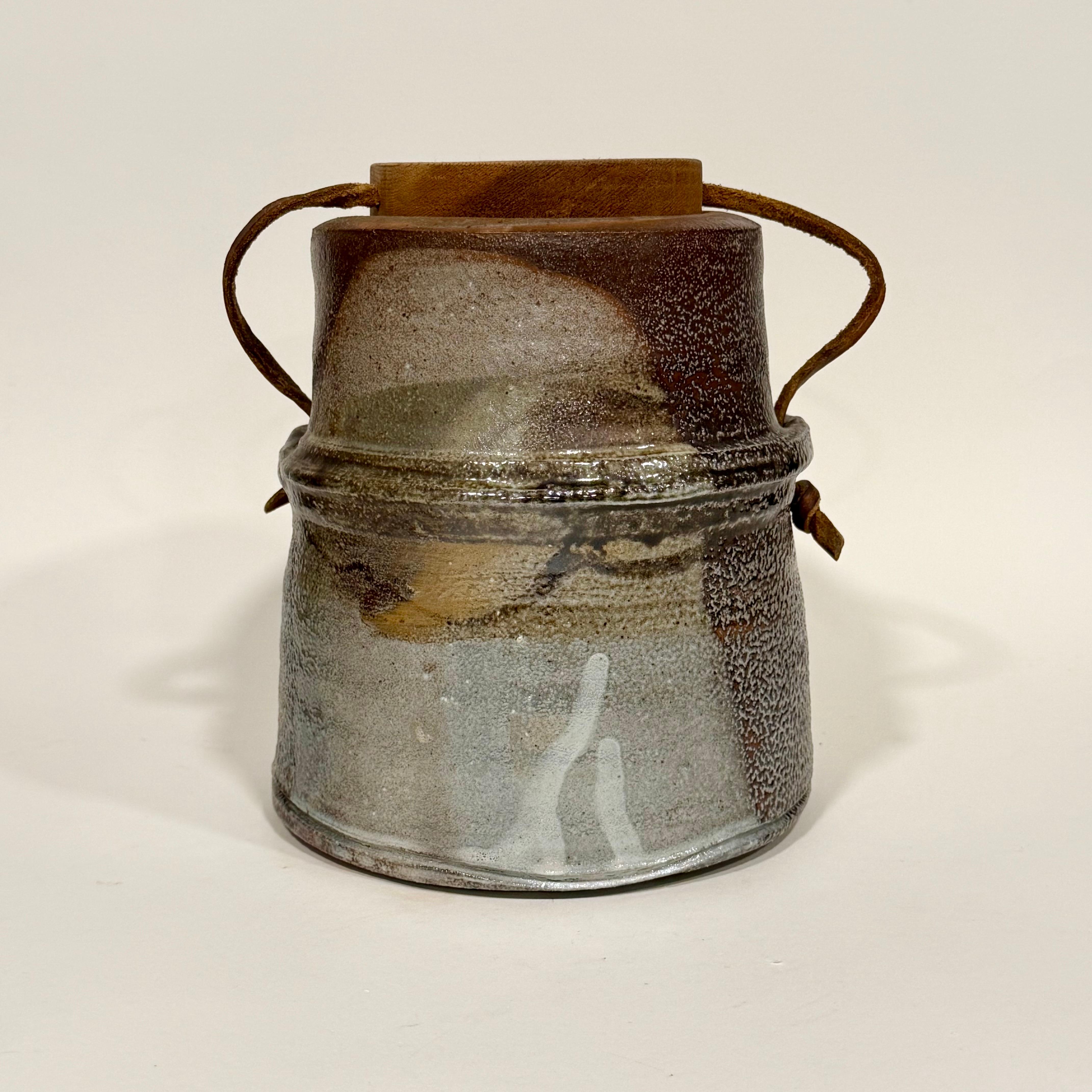 Asombrosa vasija abstracta con tapa, cocida con sal, de la alfarera Sandra Johnstone, c. 1970. Tapa de madera maciza con cordón de cuero que la sujeta al recipiente. Johnstone (1936-1991) estudió con Peter Voulkos en la Universidad de Berkeley a
